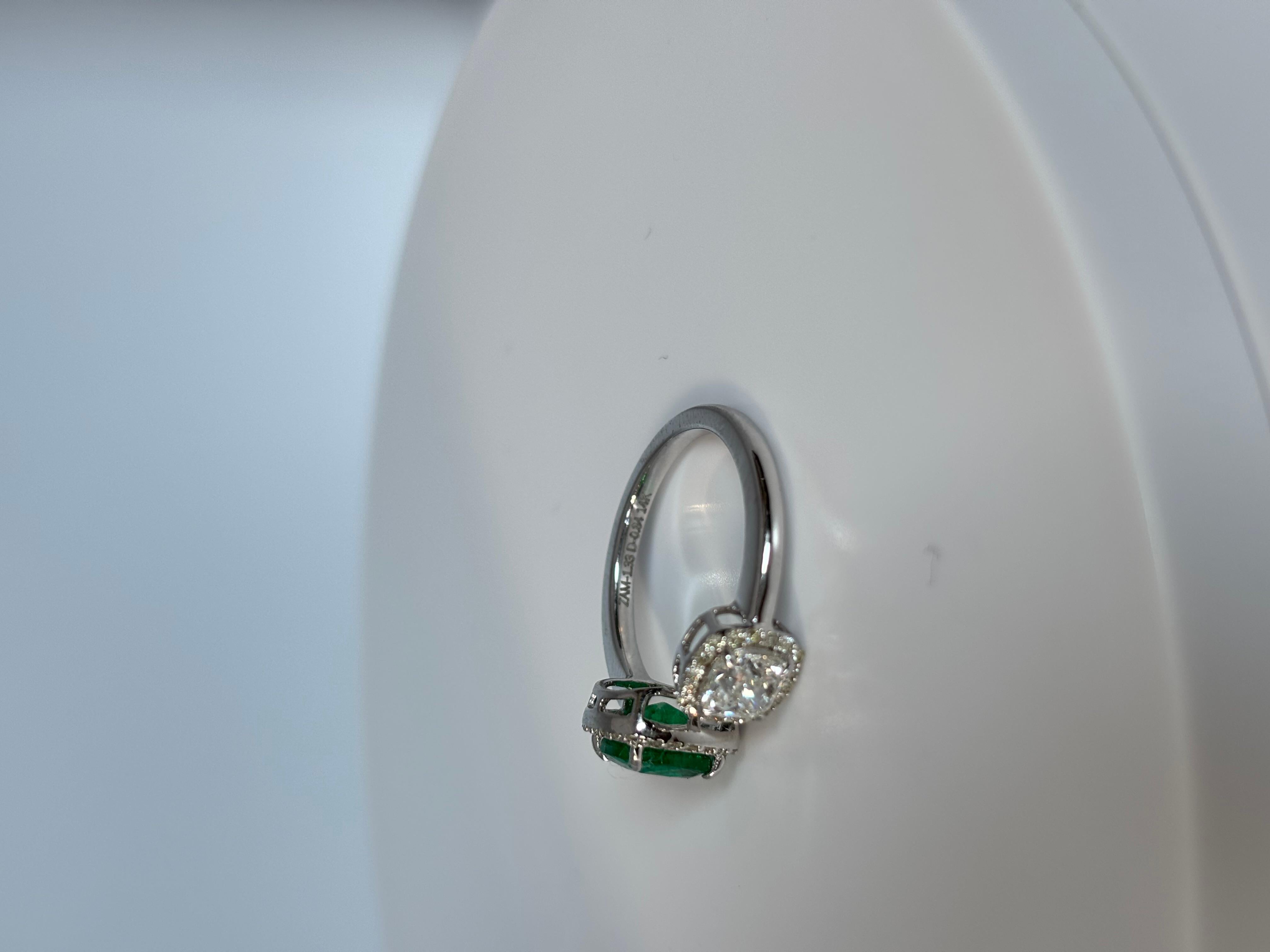Dieser atemberaubende Ring zeigt einen leuchtenden Smaragd und einen Diamanten im Kissenschliff, der von einem Kranz funkelnder Diamanten umgeben ist, die seinen satten grünen Farbton noch verstärken. Der in hochwertiges Metall gefasste Smaragd
