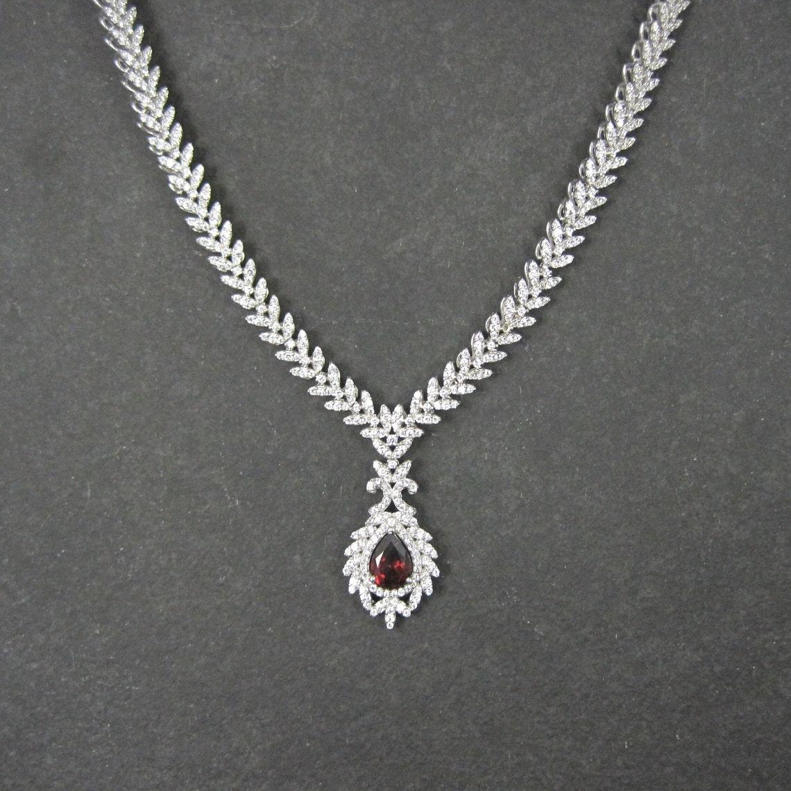 This gorgeous estate necklace is sterling silver.
It features a 6x8mm pear-cut garnet accented by cubic zirconias so beautiful that you would think they were diamonds.

This necklace measures 18 inches plus an additional 2-inch extension for 20