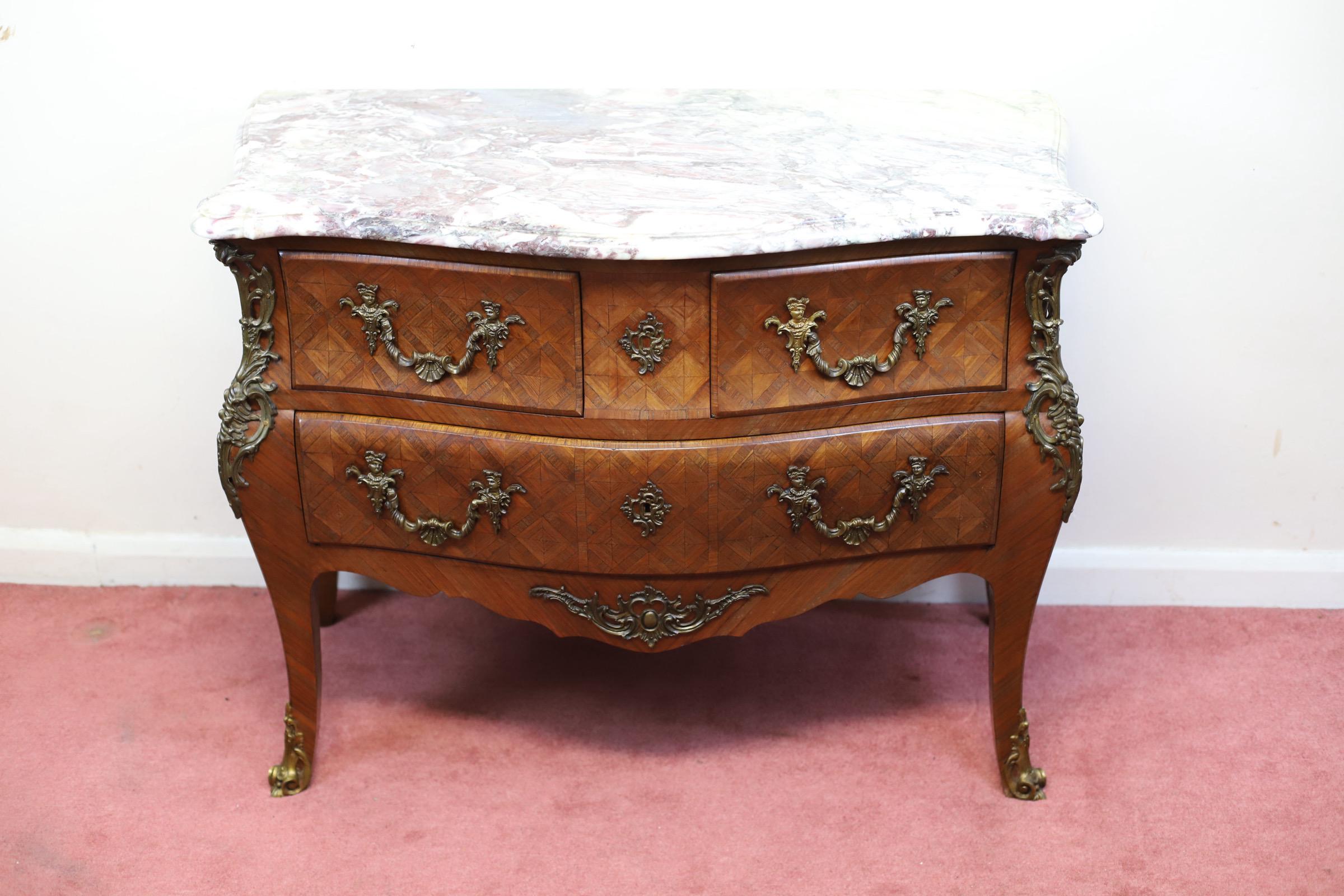 Siamo lieti di offrire in vendita questo straordinario esemplare di noce francese dell'inizio del XX secolo.  comodino a tre cassetti impiallacciato in parquet, piano in marmo sagomato sopra un corpo bombato graduato con montature in ottone, in