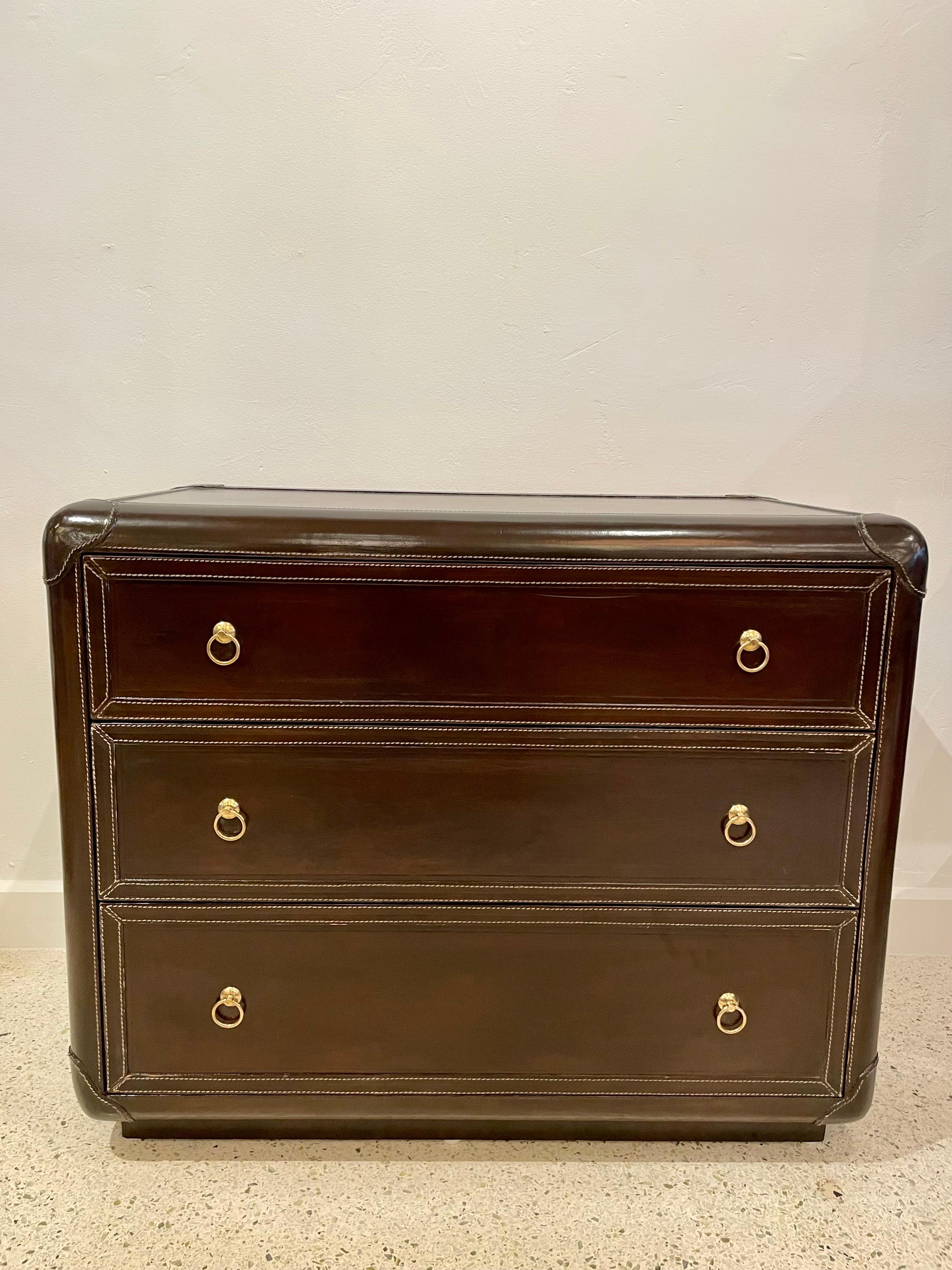 This all leather clad cabinet with exquisite stitching throughout has 3-ample paper-lined drawers and original brass pulls. The dark brown coloring of the leather and the white stitch make this piece VERY special. This is a very masculine, trunk
