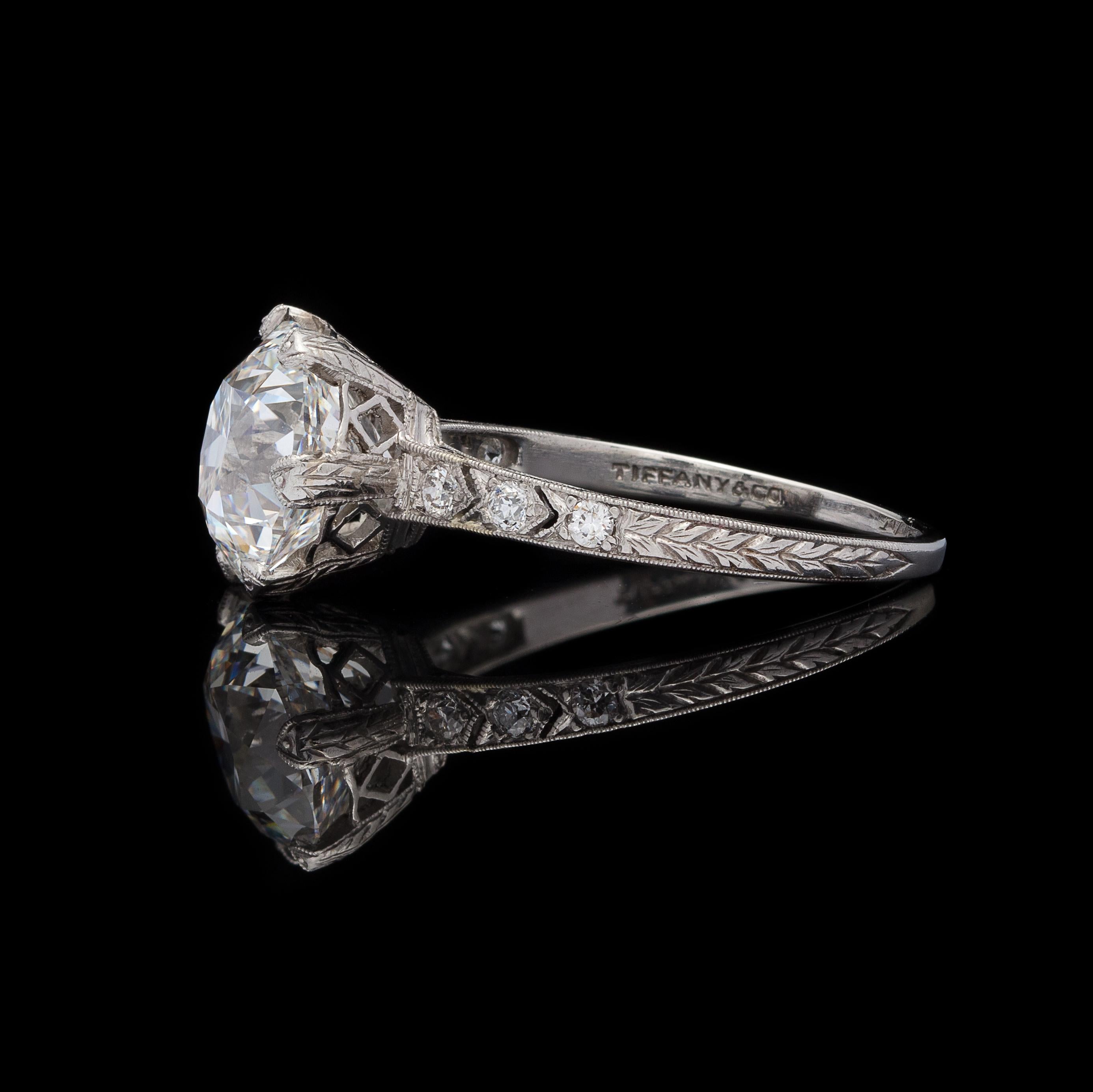 A gorgeous platinum ring, the GIA graded 3.11-cts F/VVS1 European-cut diamond is traffic stopping. Set in a glamorous, old world mounting signed Tiffany & Co.,  with open work and hand engraving, the shoulders set with 6 smaller European-cut