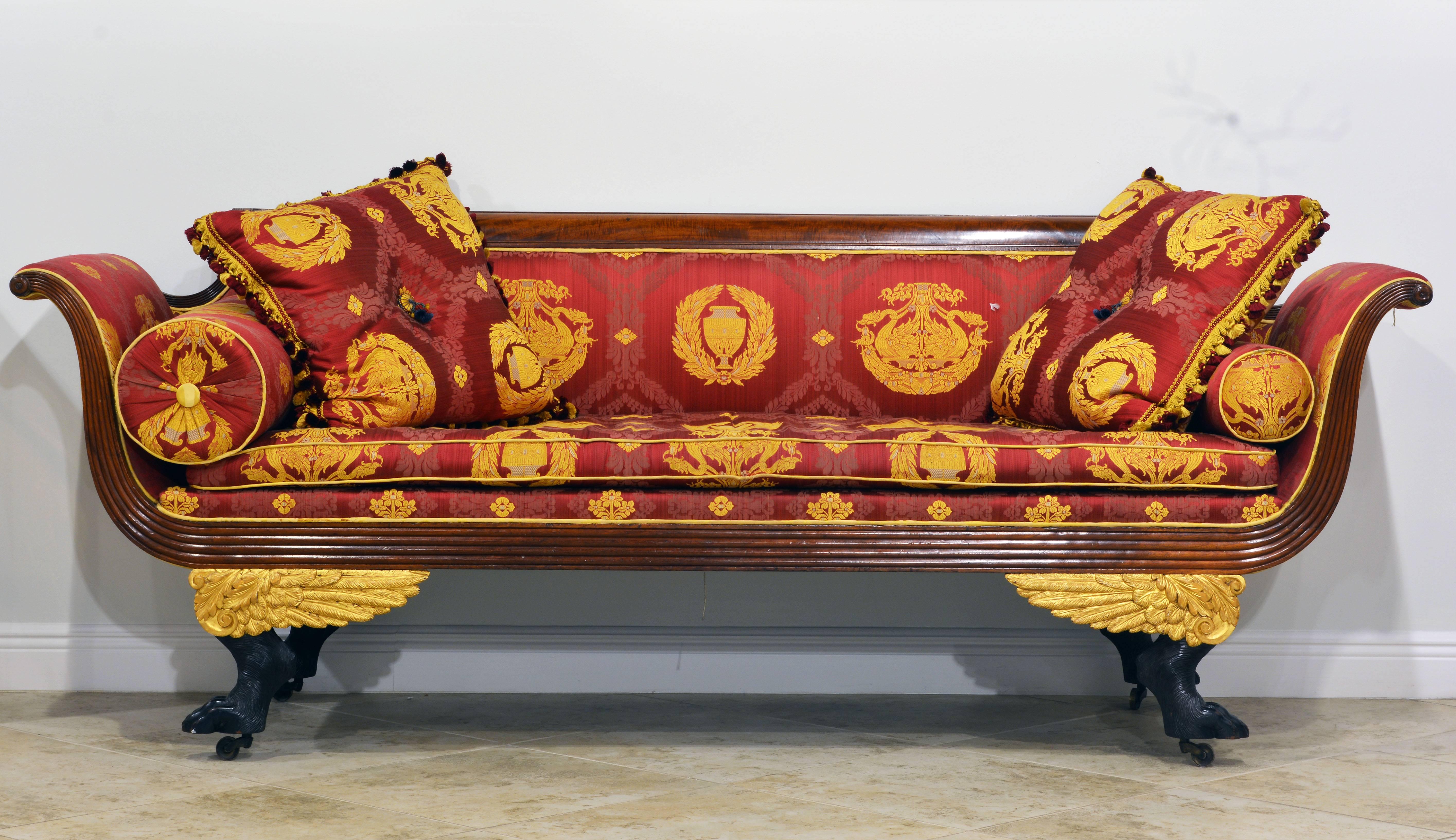 A stunning sight. The first period American classically fashioned Empire sofa (Like New York) with carved Paw legs and gilt wood wings covered by a bold Napoleonic Gianni Versace designed fabric in red and gold.