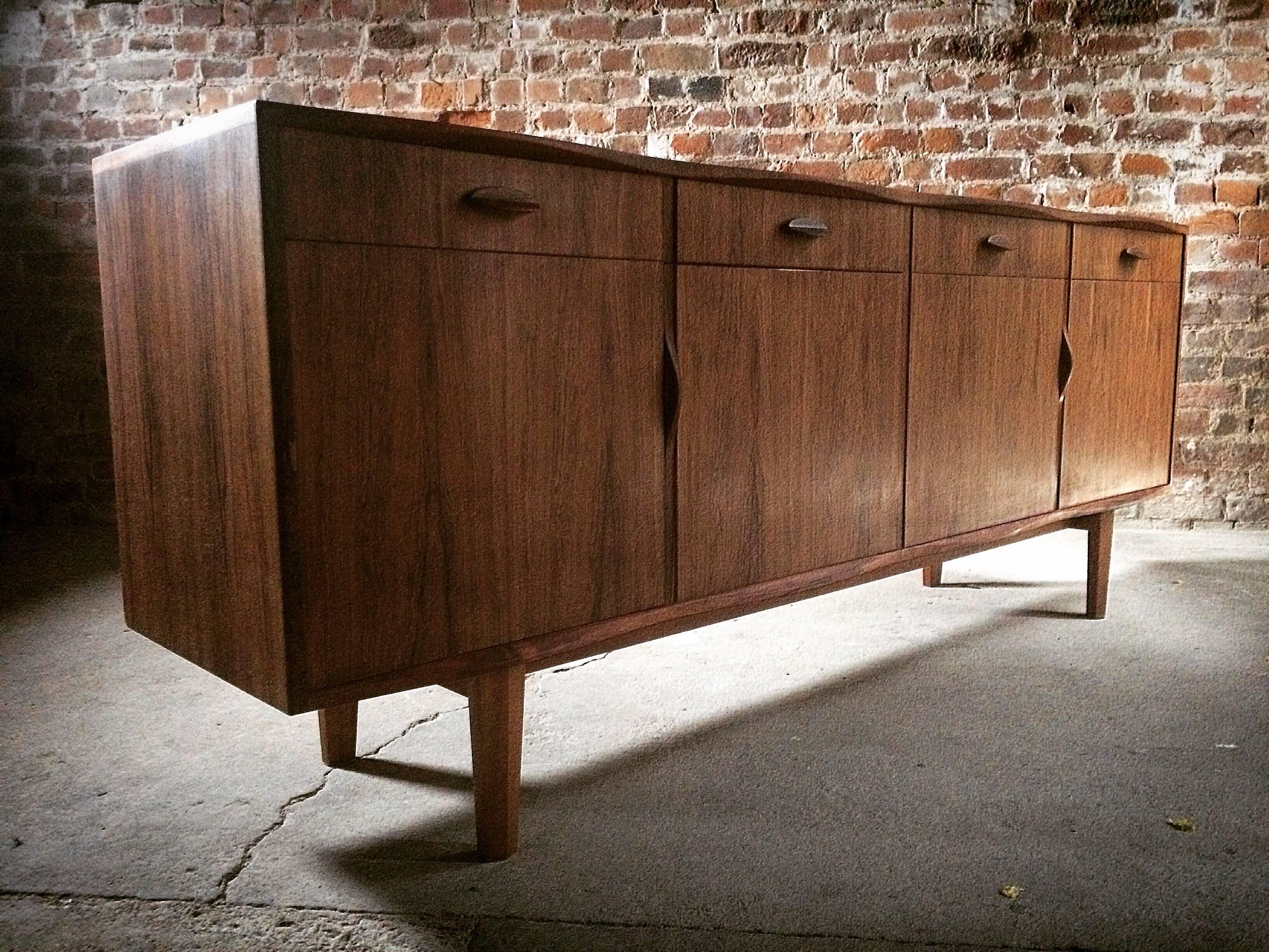 A magnificent quality and very rare Gordon Russell R818 rosewood credenza or sideboard designed by W.H. Russell FSIA, circa 1965, the serpentine top with a scalloped edge over four frieze drawers with four cupboards below, raised on four short legs,