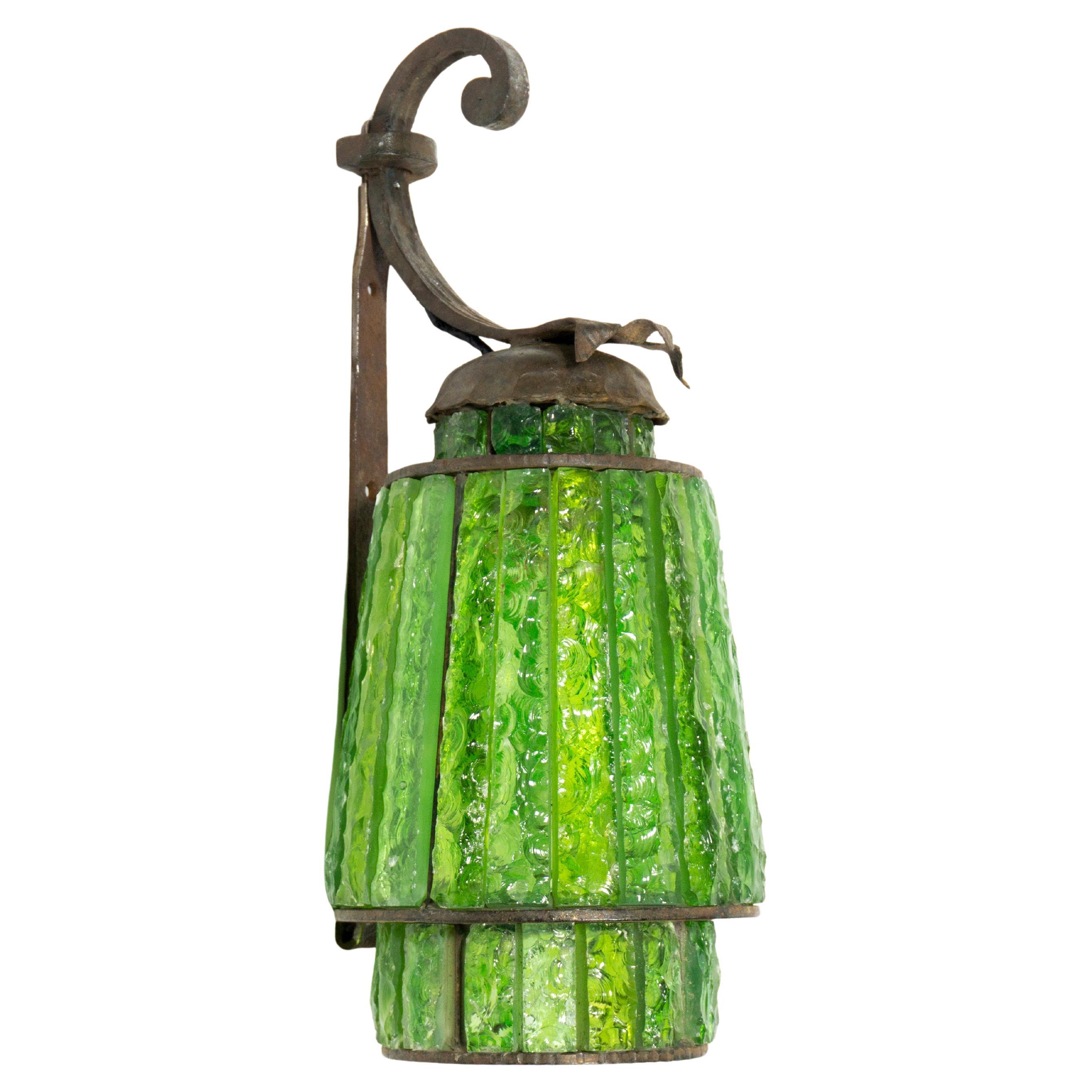 Stunning handcrafted wrough iron lantern shaped wall light / sconce with green coloured hammered glass.
The shade of the lamp is covered all round with green hammered glass elements which create a wonderful play of colours due to the slightly