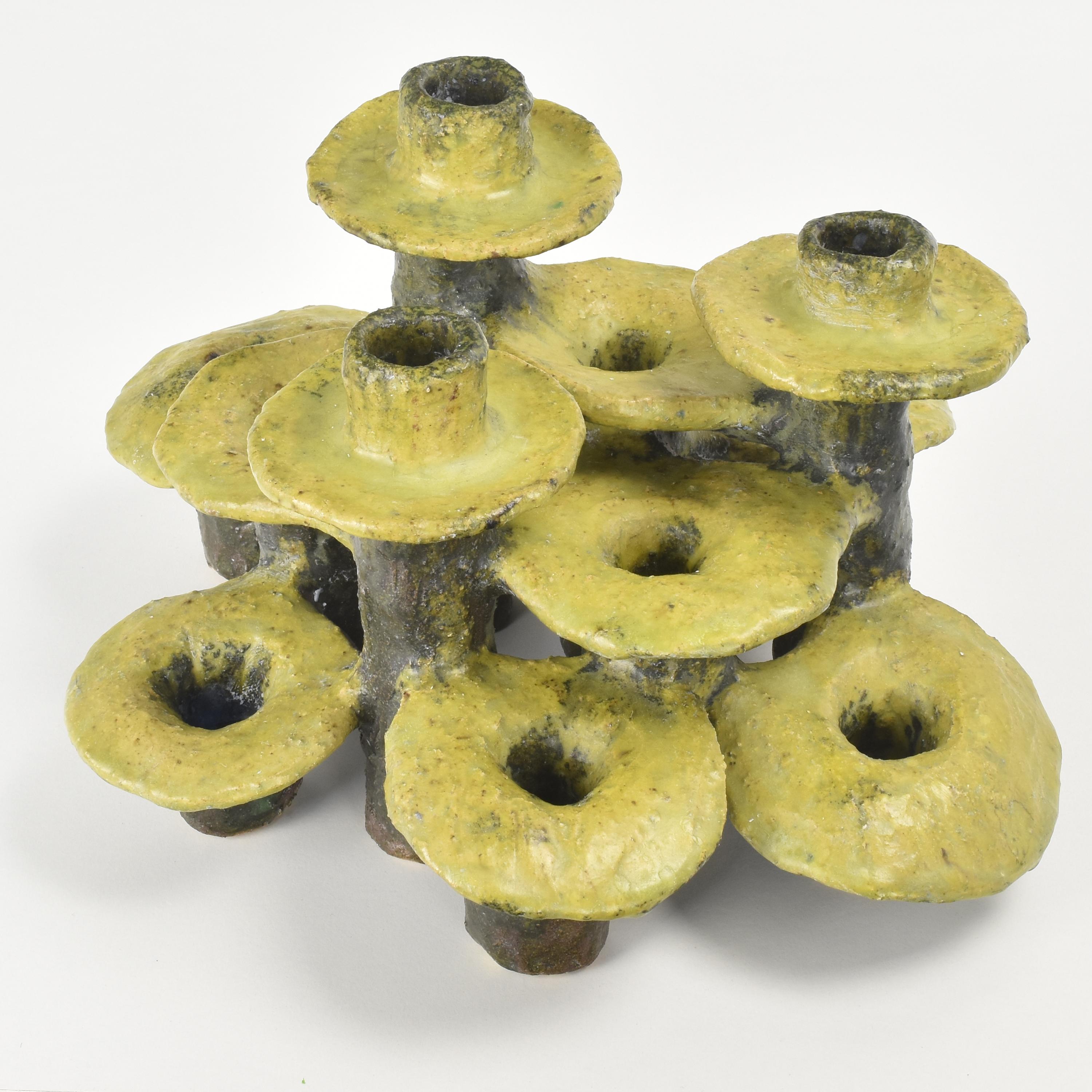 This brutalist object has a unique and creative design, featuring an arrangement of 12 candle holders, each in the shape of a mushroom, arranged in different levels to create a visually appealing composition. The overall look is reminiscent of the