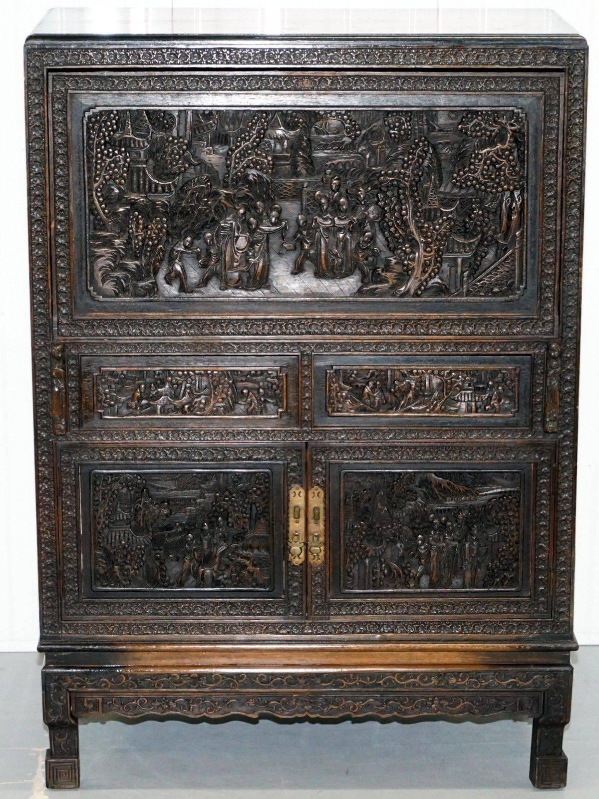 We are delighted to offer for sale this stunning antique Chinese heavily carved cabinet with drop front desk

A truly stunning piece, carved from every single inch, the drop flap supports which are finished with noble looking figures pull forward