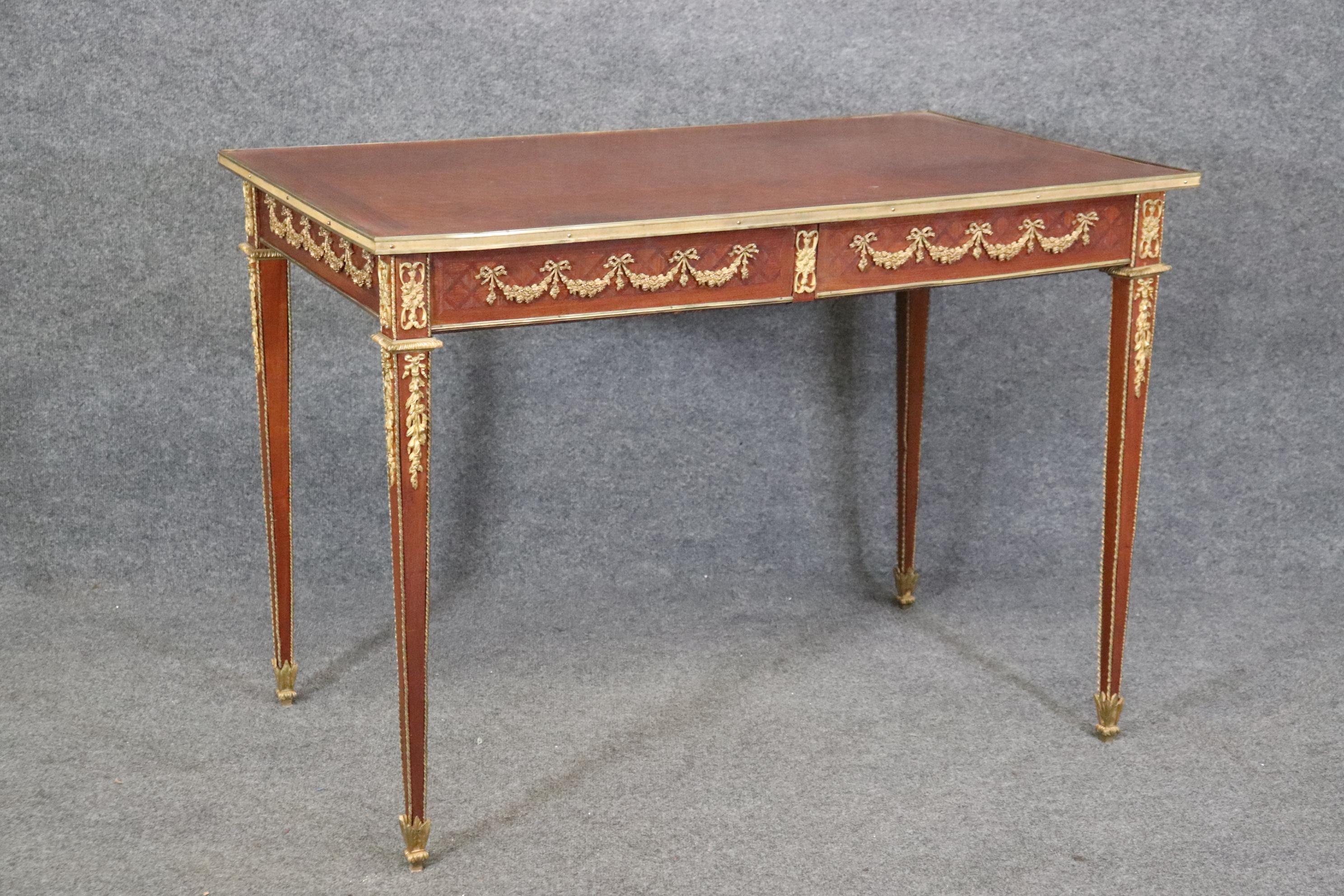 This desk is absolutely stunning with gorgeous mahogany done in marquetry inlay and bright bronze ormolu that is crisp and extremely well defined. The desk has two drawers and wll show darker areas on top from age and use. The finish is an older