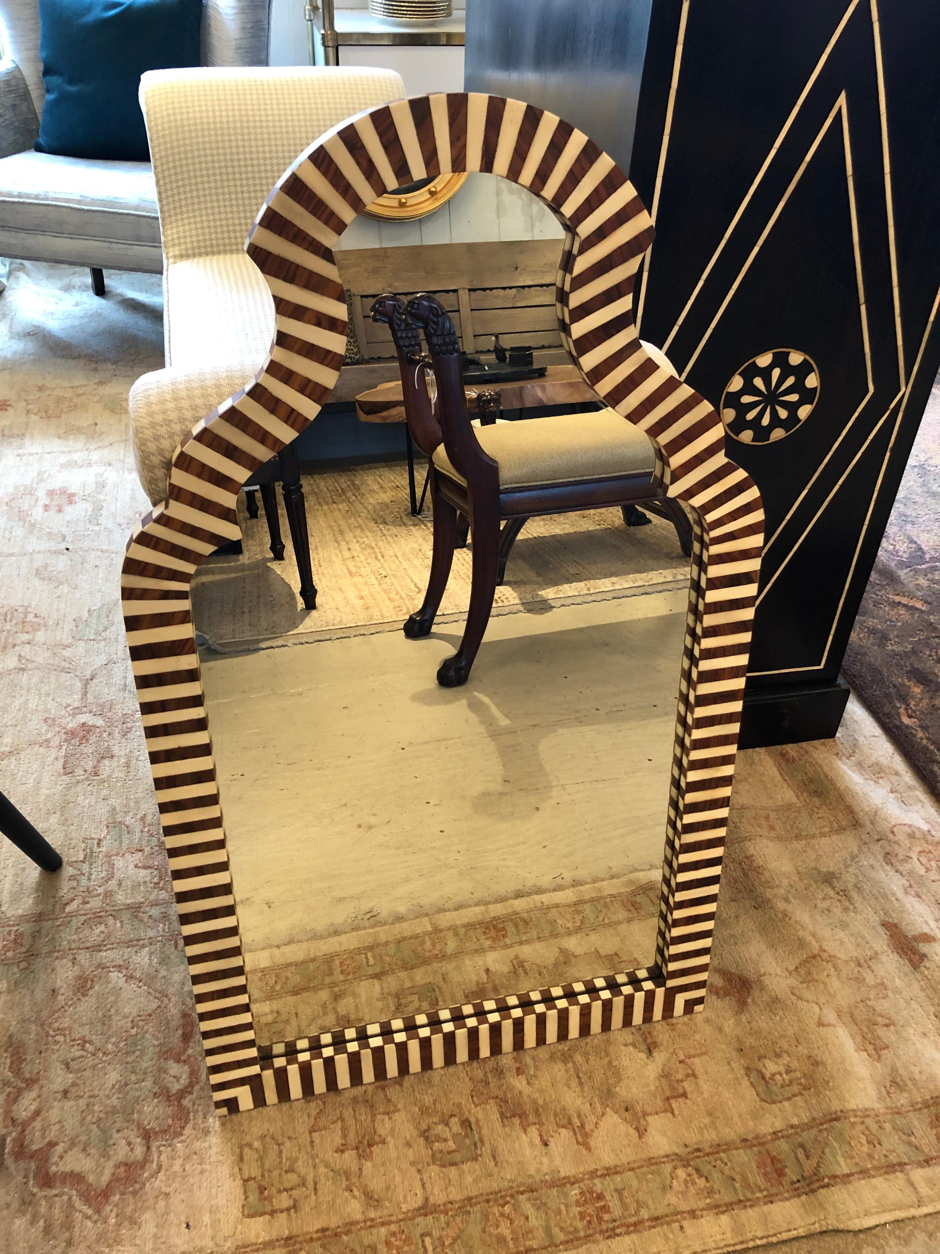 Eye catching graphic inlaid mirror by Made Goods having wonderful sculpted shape and alternating lines of rosewood veneer and bone around the frame.  Has a Moroccan vibe.
