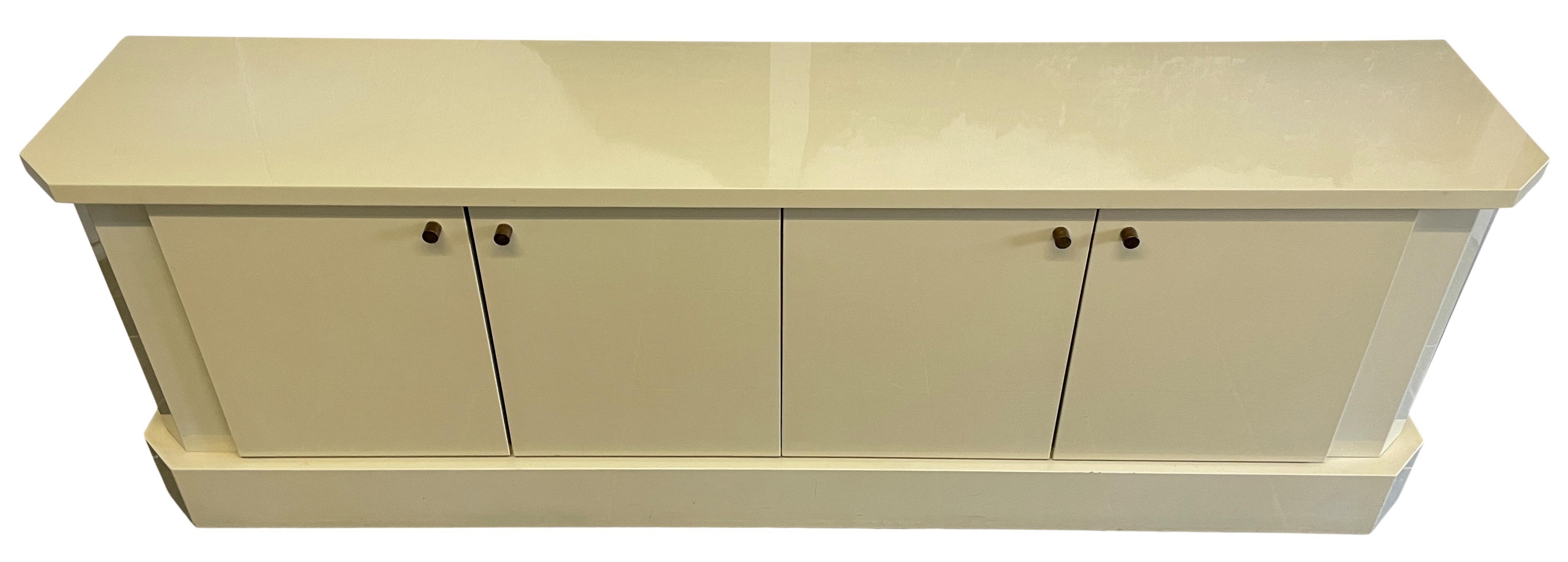 Stunning credenza by Jean Claude Mahey. Has 4 front doors with brass pulls Ivory lacquer finish. High Quality built credenza with 4 cabinet doors with solid brand cylindrical knobs. Interior is white oak wood with adjustable shelves. Very clean