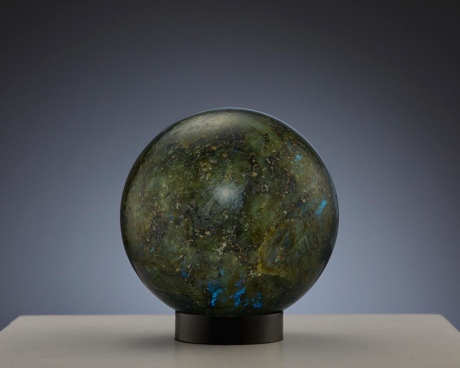 Questa splendida sfera è realizzata in Labradorite, un minerale ipnotico famoso per il suo straordinario gioco di colori, noto come labradorescenza. La sfera presenta prevalentemente una tonalità di verde, completata da spettacolari scorci di blu