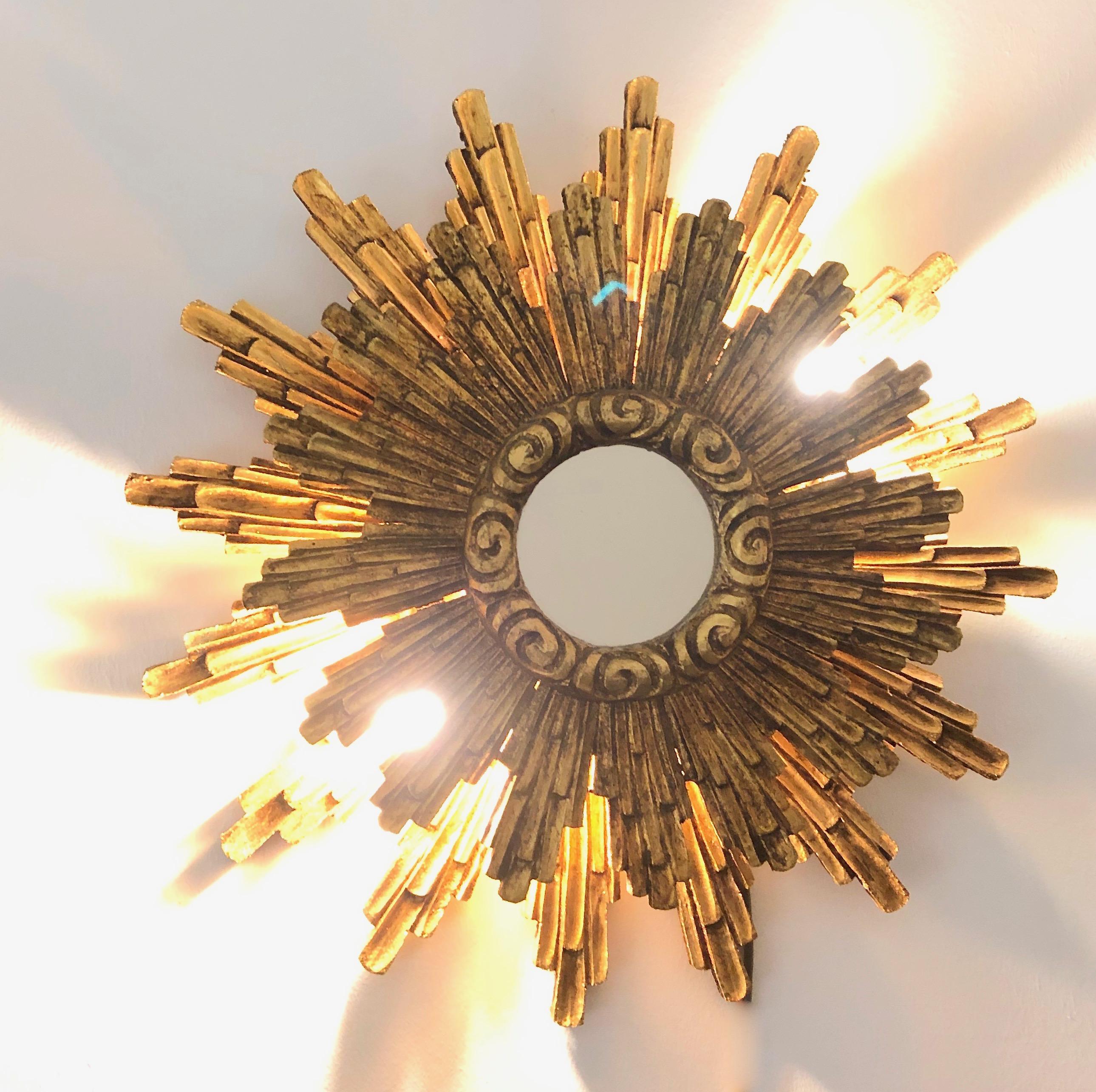 A stunning large starburst mirror, illuminated at the backside with two European E14 / 110 Volt candelabra bulbs, each bulb up to 40 watts. Made of gilded wood. Original as found condition (see all the detailed pictures). It measures approximate 23
