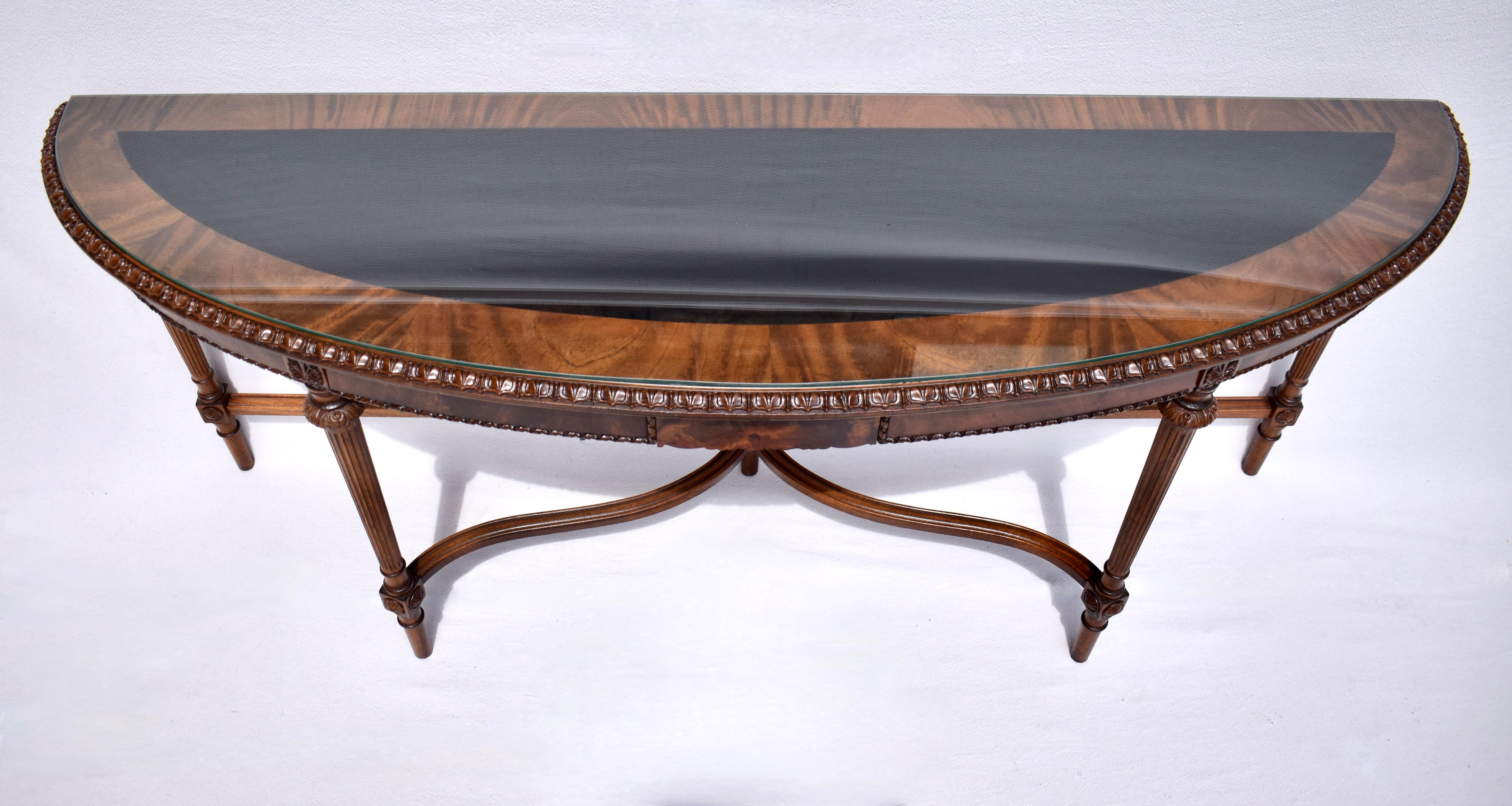 Long Louis XVI style Demi Lune Console table with two pocket drawers accented with carved details throughout, exquisite fiery Mahogany wood grains, resting on five reeded tapered legs & serpentine stretcher. Includes custom polished edge glass top.