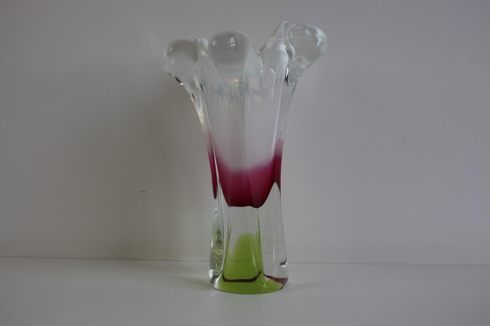 This striking hand-blown art glass vase, likely of Czech origin and dating to the mid-20th century, features an elegant organic form with a flared rim and sculptural folds. The body is crafted from clear glass infused with vibrant internal coloring