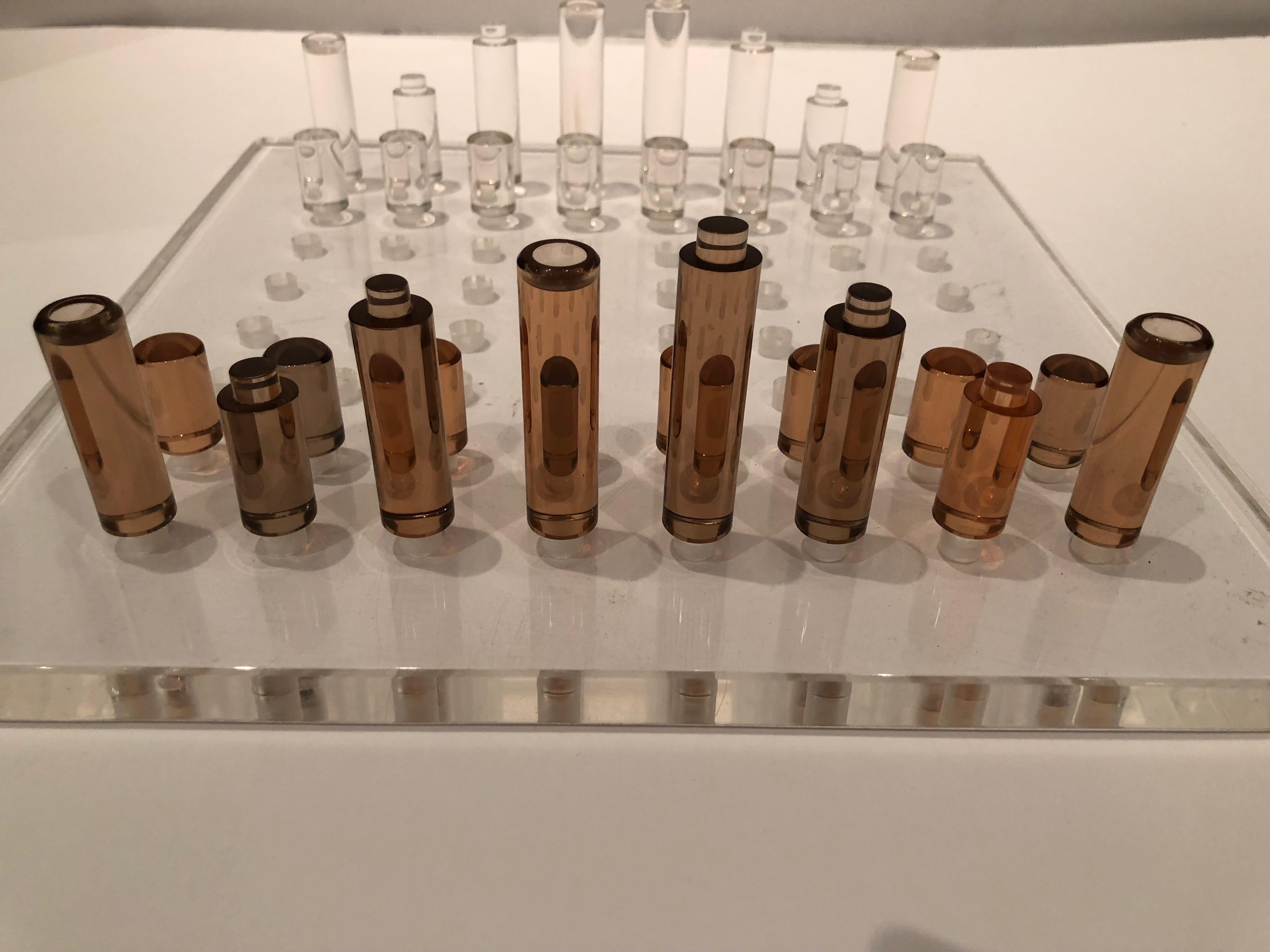 Mid-Century Modern Lucite chess set in a unique design. Each chess piece is pegged and fits into holes in the Lucite board. Half are transparent while the opposing pieces are amber in color. Board is .75 thick. Chess pieces are 3 inches, 1.75 and