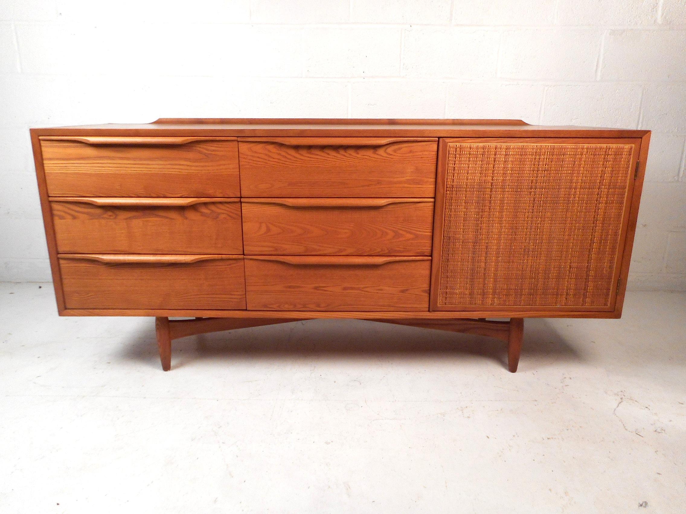 This impressive midcentury dresser features a sturdy oak construction, brilliant wood grain highlights, cross-base support, six drawers and three sliding trays behind a woven cane cabinet door offering ample storage space, circa 1960s made by Oskar