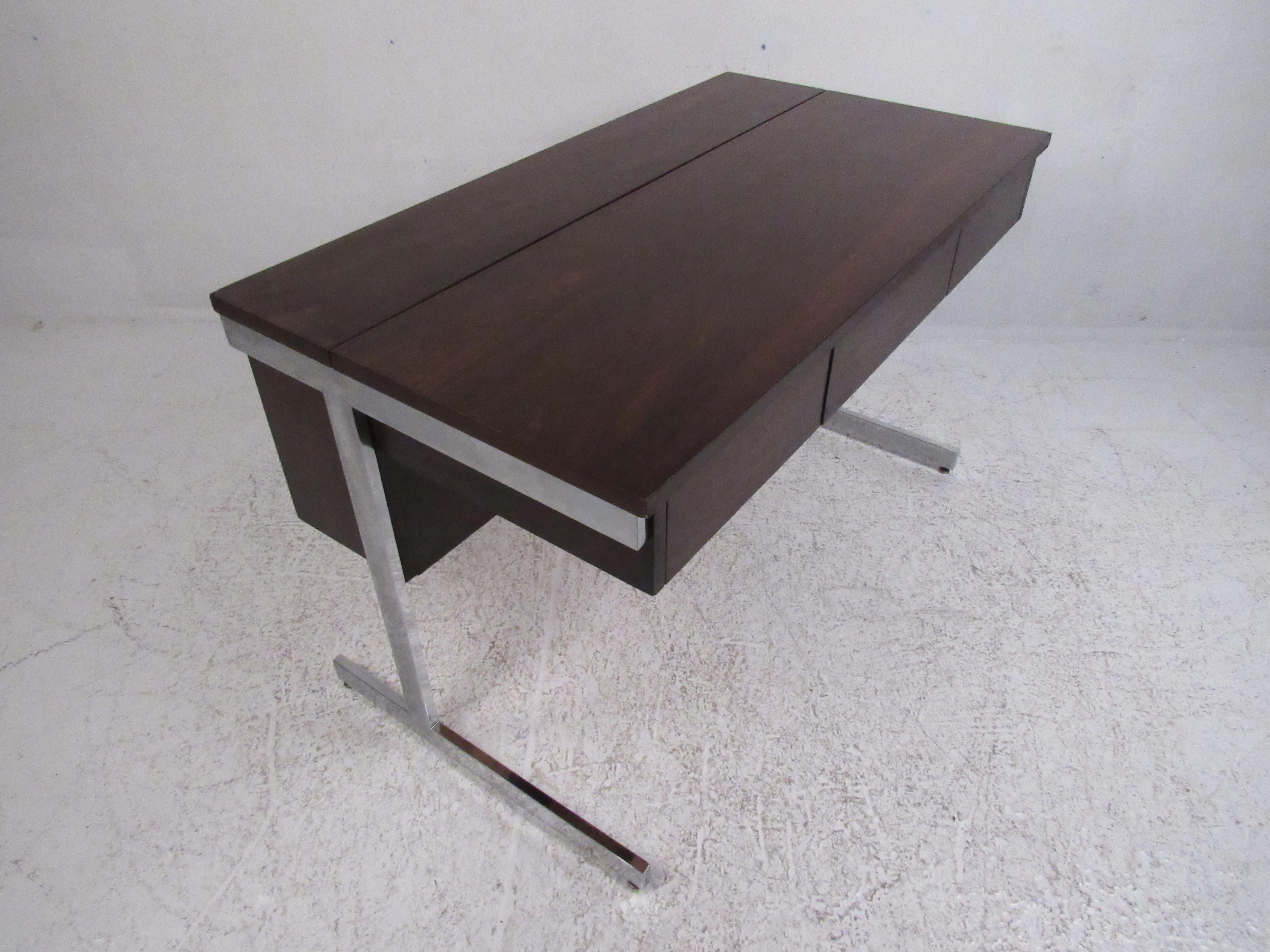This attractive vintage modern desk features a unique pop-top storage compartment on the top and three large drawers. A one of a kind design with chrome flat bar sled legs and elegant rosewood grain throughout. This well-made case piece has a