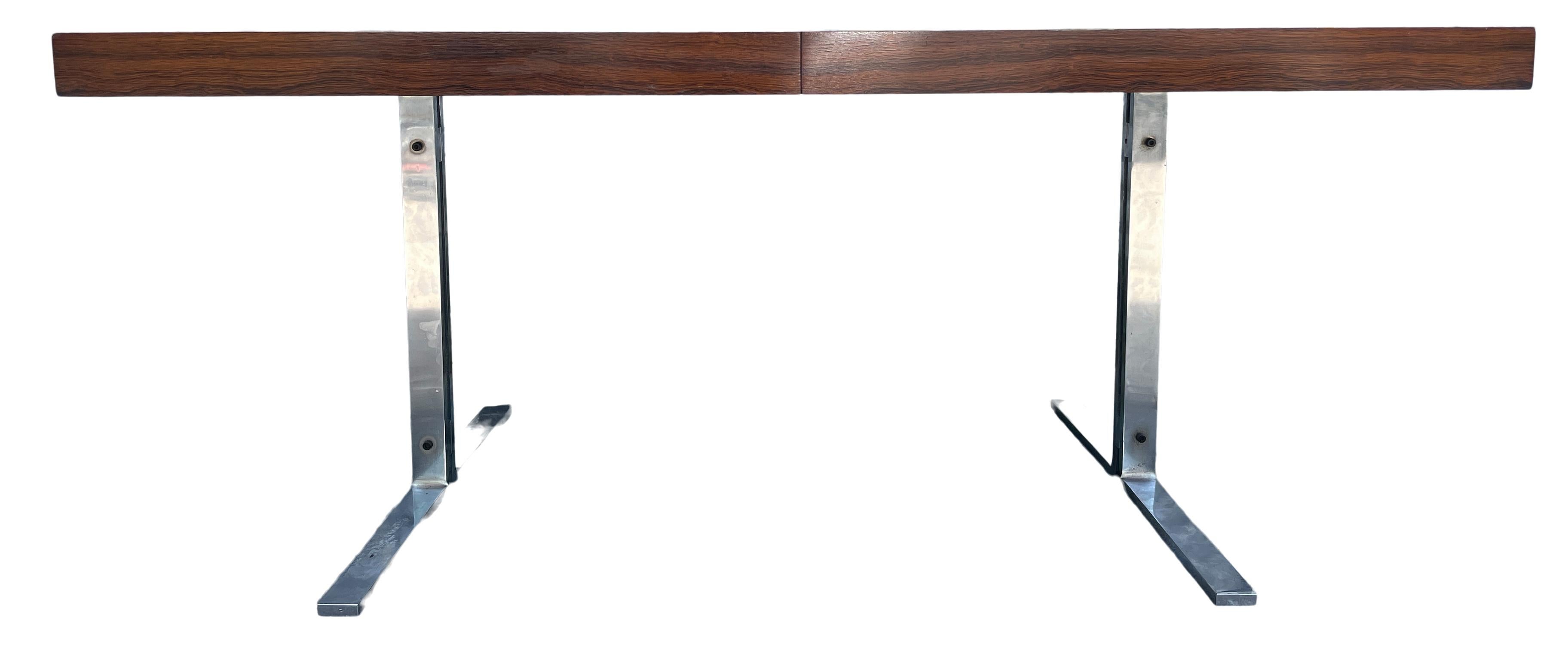 Magnifique table de salle à manger rare en palissandre brésilien avec un plateau de forme rectangulaire sur des pieds chromés. La table à manger a une feuille qui est amovible et se range sous la table. La feuille est un peu plus foncée en raison de