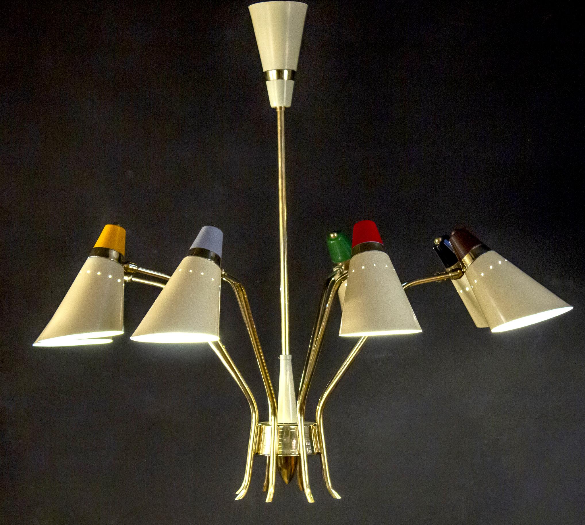 Singolare lampadario iconico Stilnovo, caratterizzato da otto bracci rotanti, ognuno dei quali sostiene i paralumi laccati avorio e multicolore, traforati.
Elegante cornice centrale in ottone.
Questo lampadario è in ottime condizioni originali e