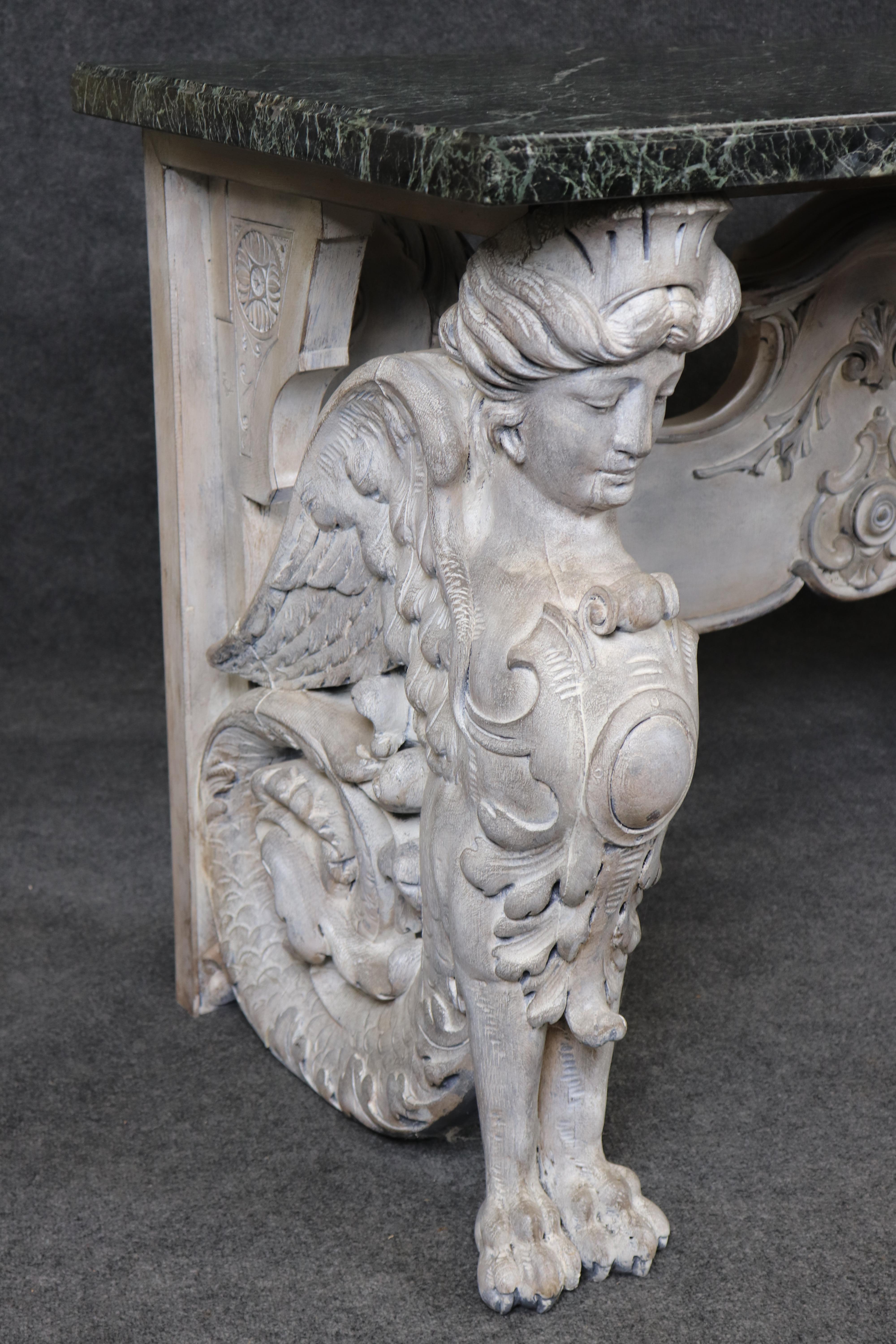 This is a fantastic and monumental carved walnut paint decorated console table. The table features a gorgeous verdi marble slab on top of a mythical maiden sphinx base with cabachon carved details and tails. The table is in a distressed antique