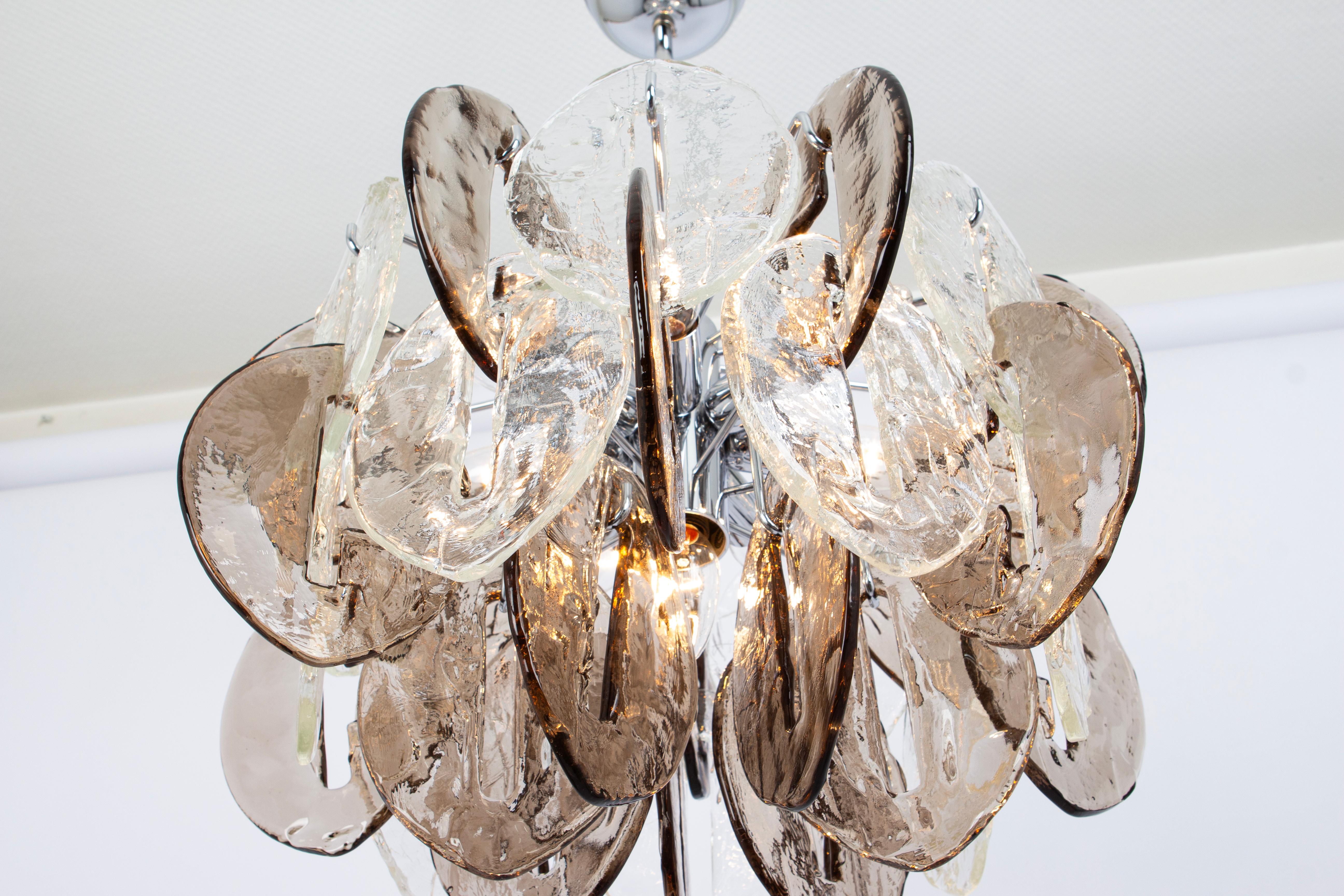 A stunning Large Murano glass Chandelier designed by Carlo Nason for Kalmar, Austria, manufactured in the 1970s. (Serie: CEO)
The Chandelier is composed of 35 thick textured glass elements attached to a chrome metal frame.
Elevate your surroundings