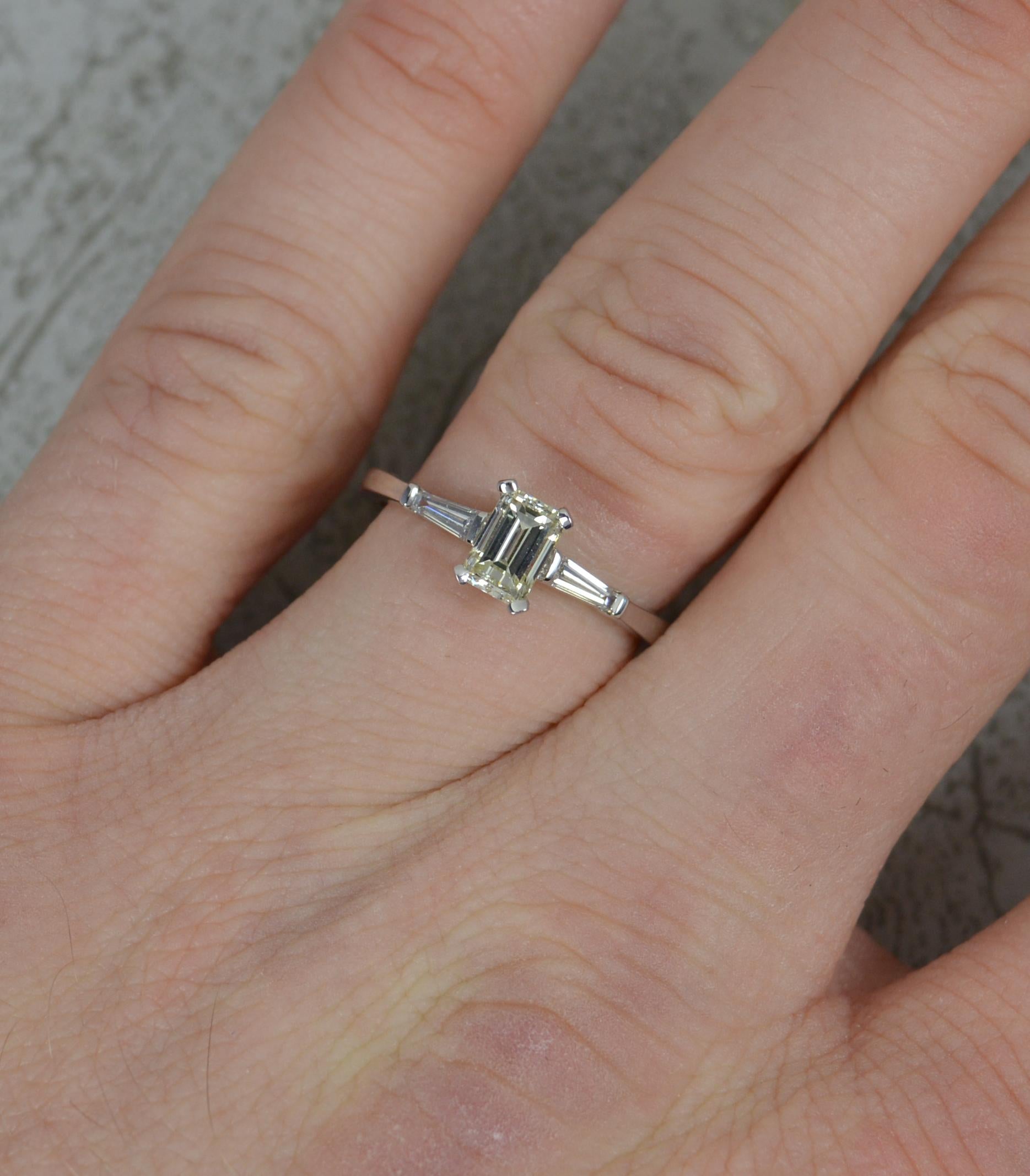 A wonderful diamond engagement ring.
Solid 18 carat white gold example.
Designed with an emerald cut diamond to centre, set into a four claw mount. 0.6cts. Vs clarity, natural light fancy yellow gold. Set with a tapered baguette cut diamond to each