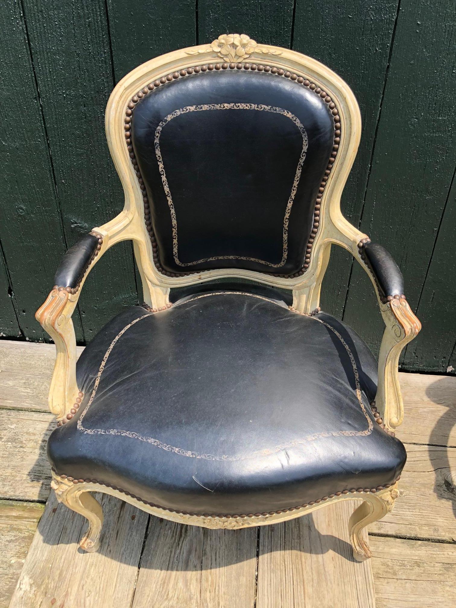 Wonderful pair of 19th century French fauteuils having cream painted carved wood frames and supple original black leather upholstery with gold embossed decoration. #4434