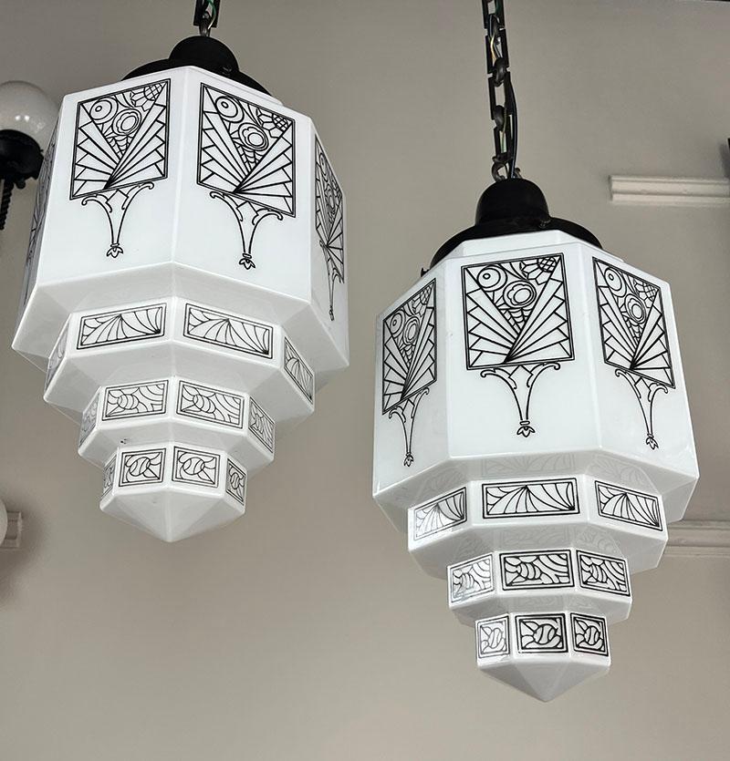 Incredible pair of matching Art Deco skyscraper pendants. Shades are in perfect condition and geometric floral pattern is crisp and clean on each panel. Holders are original and feature a lovely black patina with square and round patterned chain.