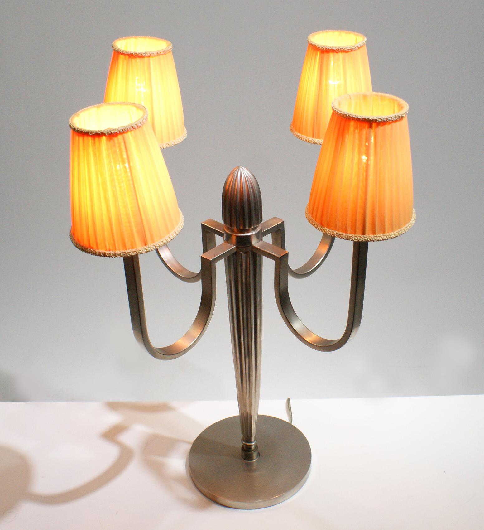 Pair of Art Deco table lamp in the style of the French artist J.E Ruhlmann, having a central column with four curved arms of lights in silvered bronze modernist design, supporting four pleated “bistro” shape lampshades in light orange linen fabric.