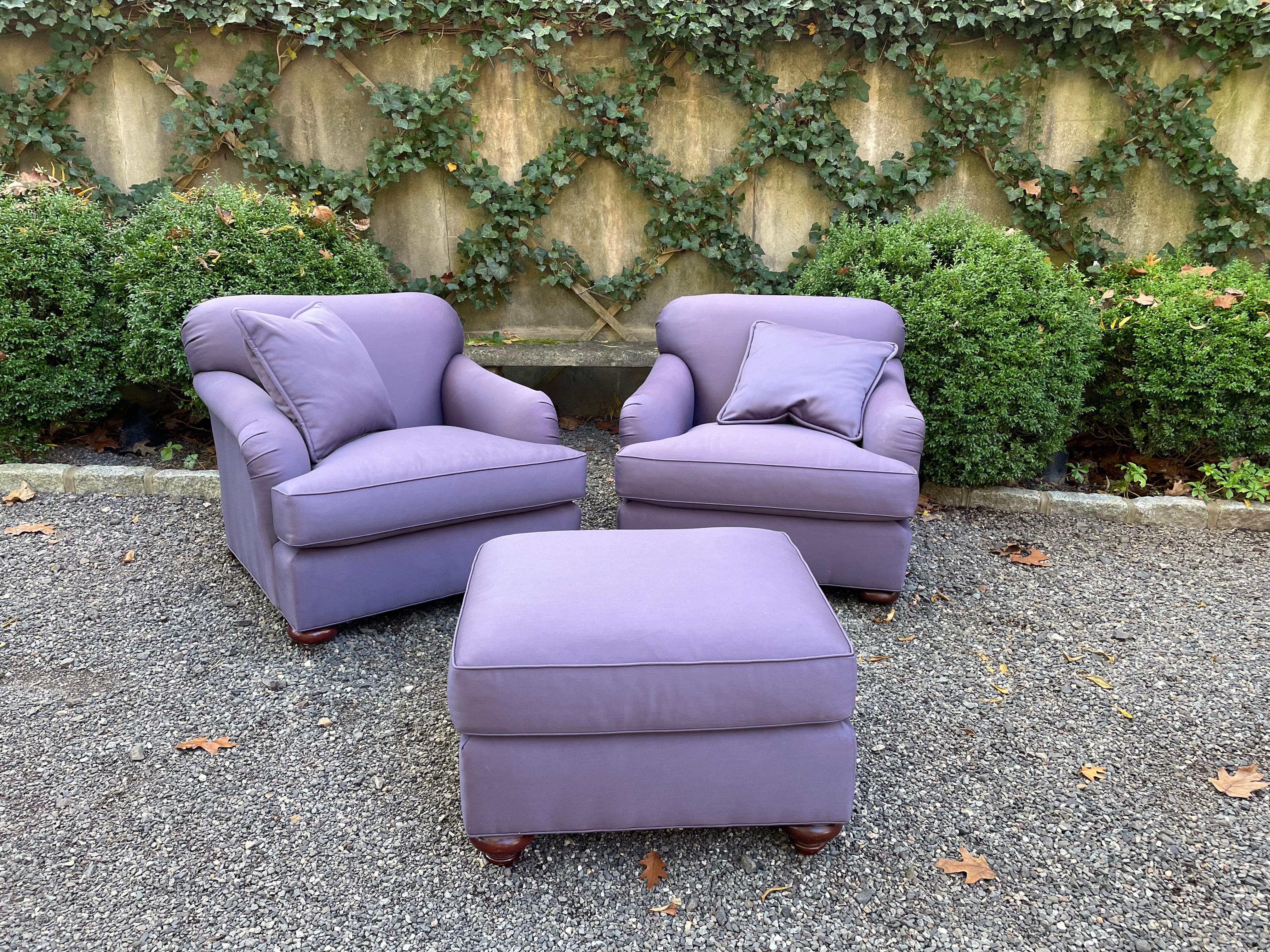 Super comfy and stylish plush pair of upholstered club chairs and matching ottoman by Baker. Upholstered in a stylish aubergine heavy weight cotton, the chairs have mahogany rounded feet in the front and splayed feet in back. The ottoman has rounded