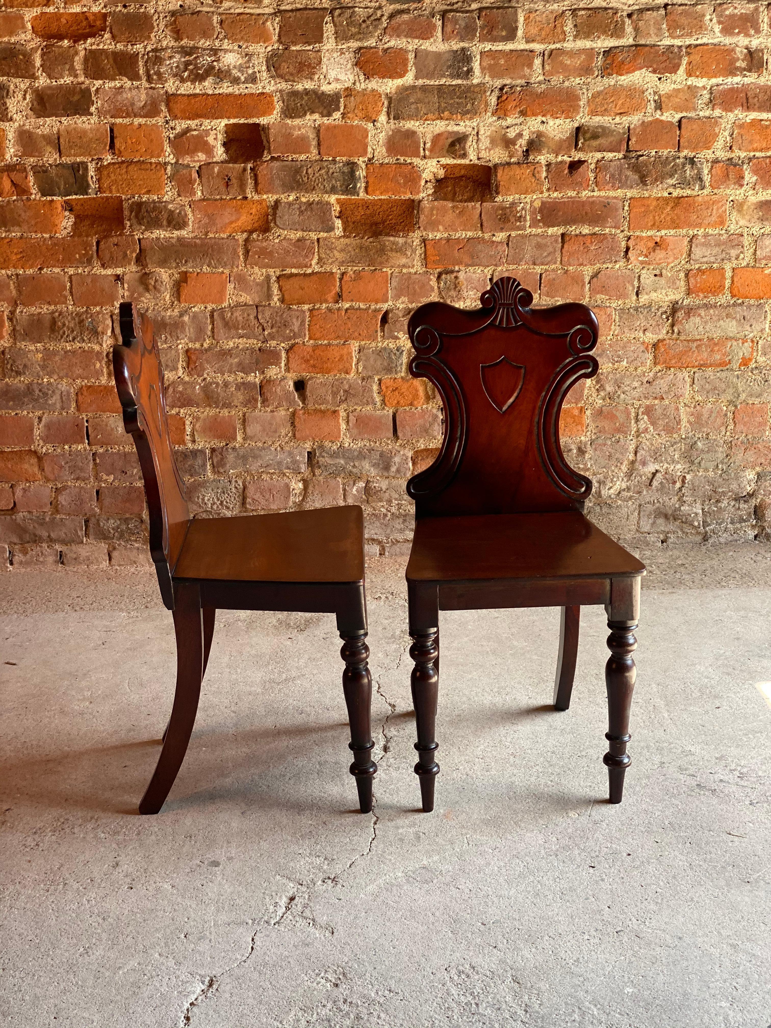 A stunning pair of early 19th century mahogany hall-chairs of fine quality timber having acquired a good color and patination; the cartouche-shaped backs carved with acanthus leaves and a central shield, the seats paneled and standing on turned and