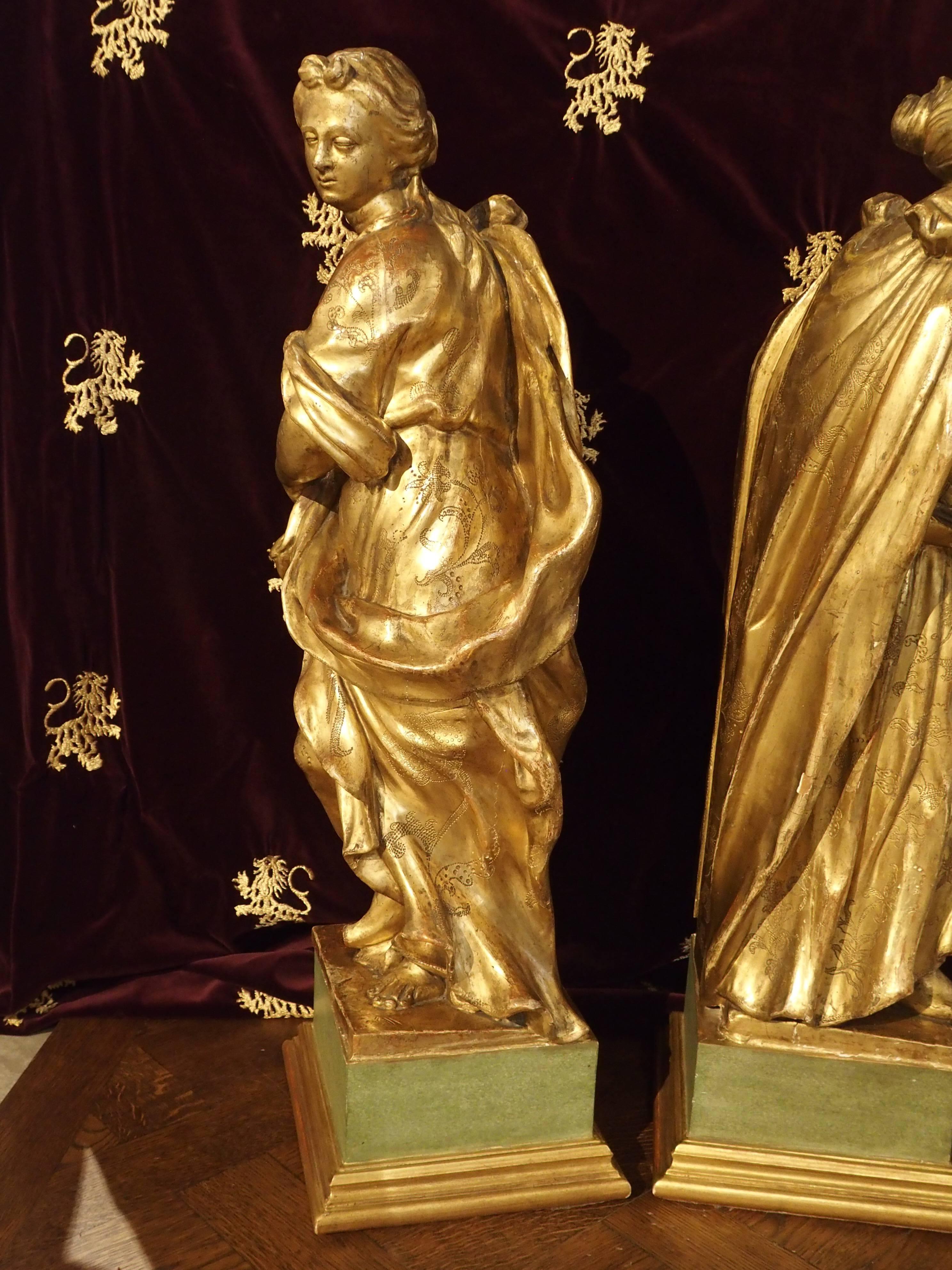 This is a spectacular pair of Italian giltwood statues featuring two women wearing impressive robes. Areas of red bole shows beneath the gilding. The carver has hand punched varying beautiful design motifs on a solid background. One woman wears a