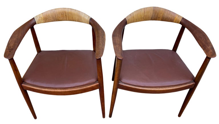 Stunning Pair of Mid-Century Modern oak leather horseshoe armchairs style of Hans Wegner. Beautiful Solid Oak chairs with a walnut brown finish - Thick Cane wrapped backrests with reddish-brown Leather seat cushions. In the style of Hans J. Wegner
