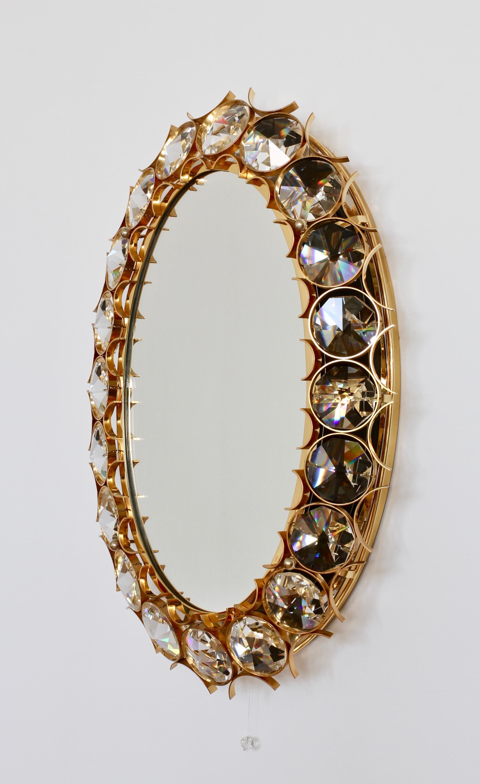 Stunning oval shaped mid-century gilt brass and crystal wall-mounted backlit vanity or hallway mirror by Palwa, Germany, circa 1965-1975. Perfect for the Hollywood Regency style, there is no better combination than gold and crystal for the opulent,