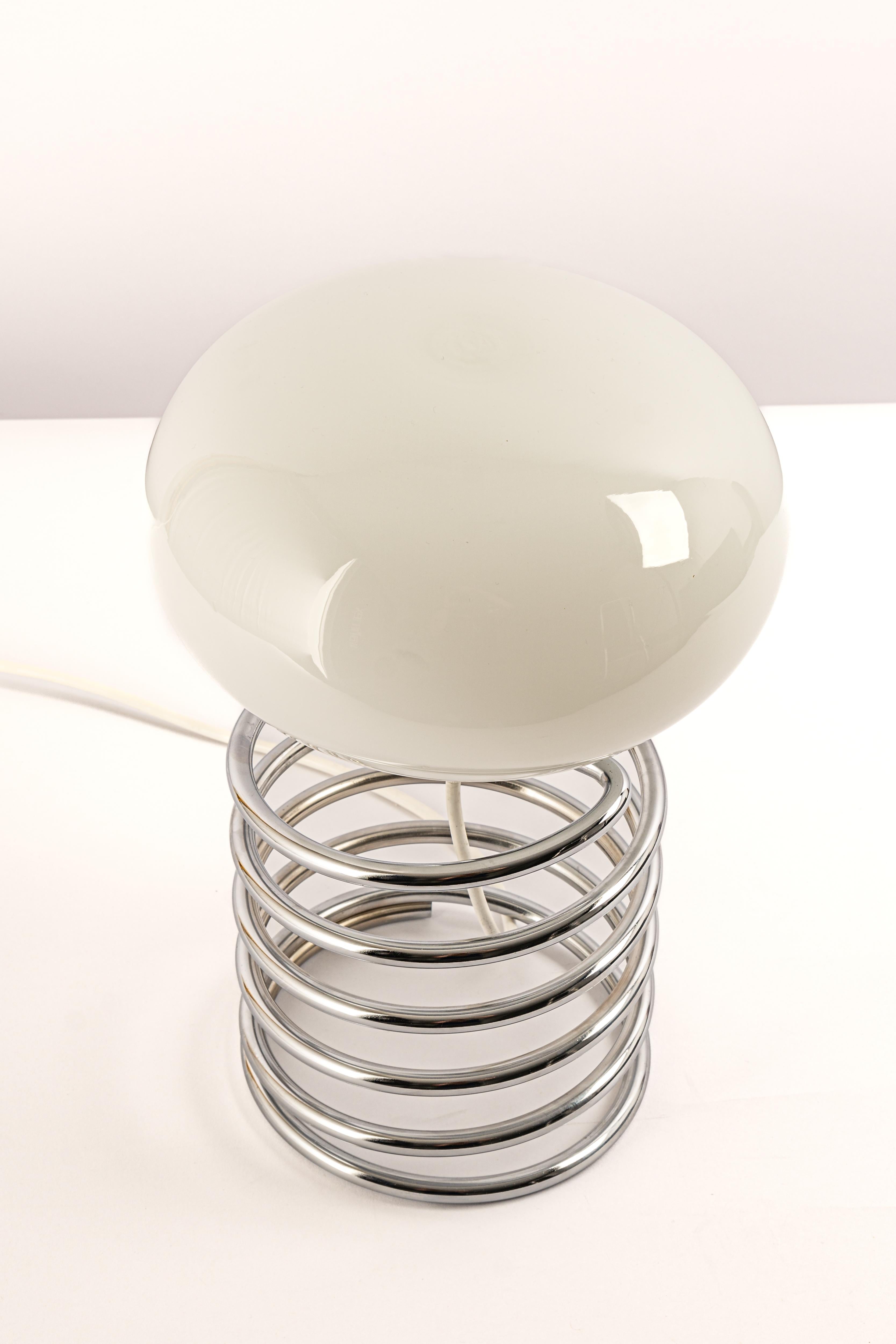 Merveilleuse lampe de table en spirale dans le style du designer Ingo Maurer, Allemagne, années 1970. 
Grande forme avec un abat-jour en verre blanc sur une base en acier spiralé chromé.

Douille : 1 x E27 ampoule standard.
Les ampoules ne sont pas