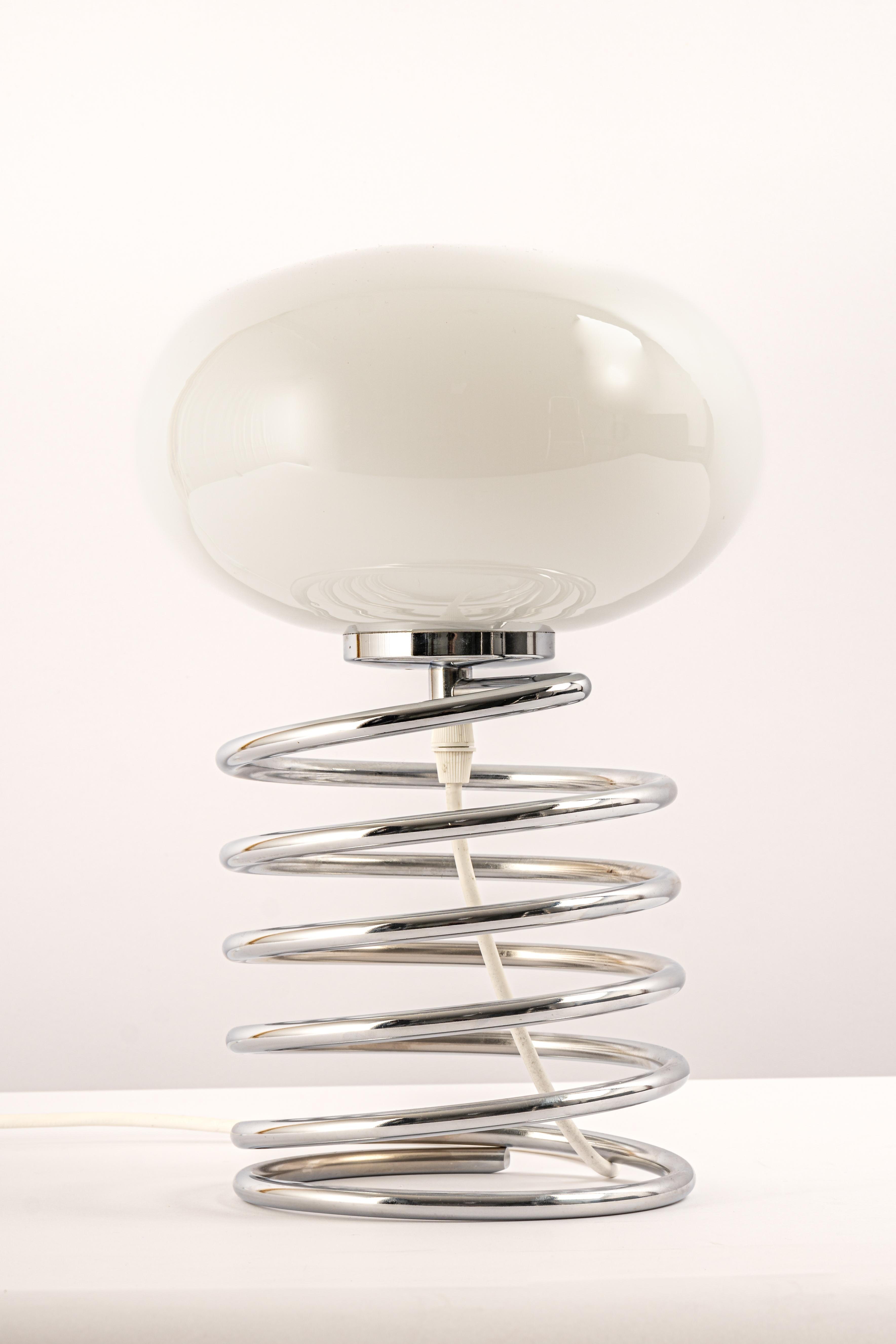 Merveilleuse lampe de table en spirale dans le style du designer Ingo Maurer, Allemagne, années 1970. 
Grande forme avec un abat-jour en verre blanc sur une base en acier spiralé chromé.

Douille : 1 x E27 ampoule standard.
Les ampoules ne sont pas