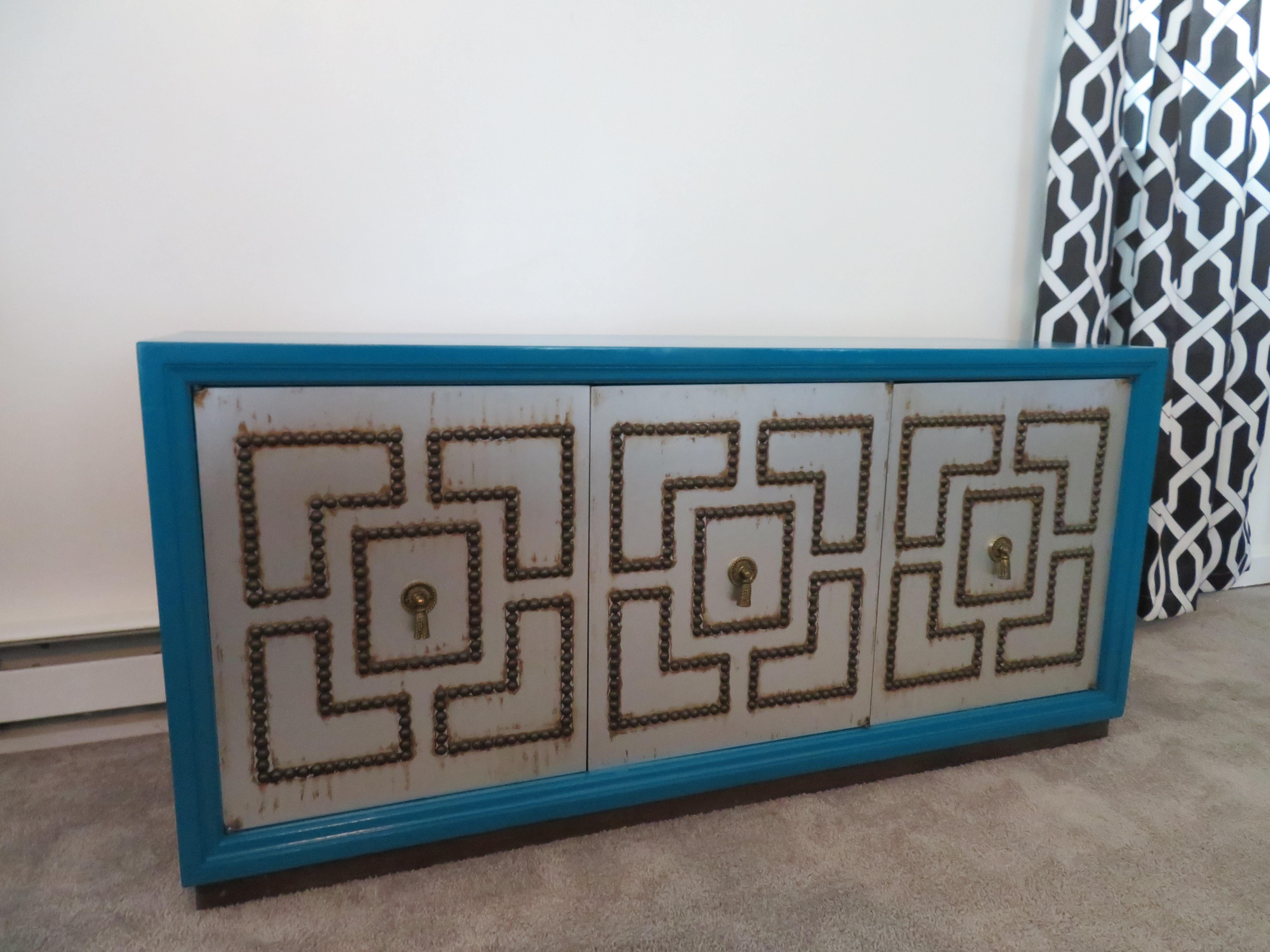 Splendida credenza in stile Parzinger con finitura dipinta a mano. Adoriamo il colore blu pavone contro i meravigliosi frontali borchiati delle porte.