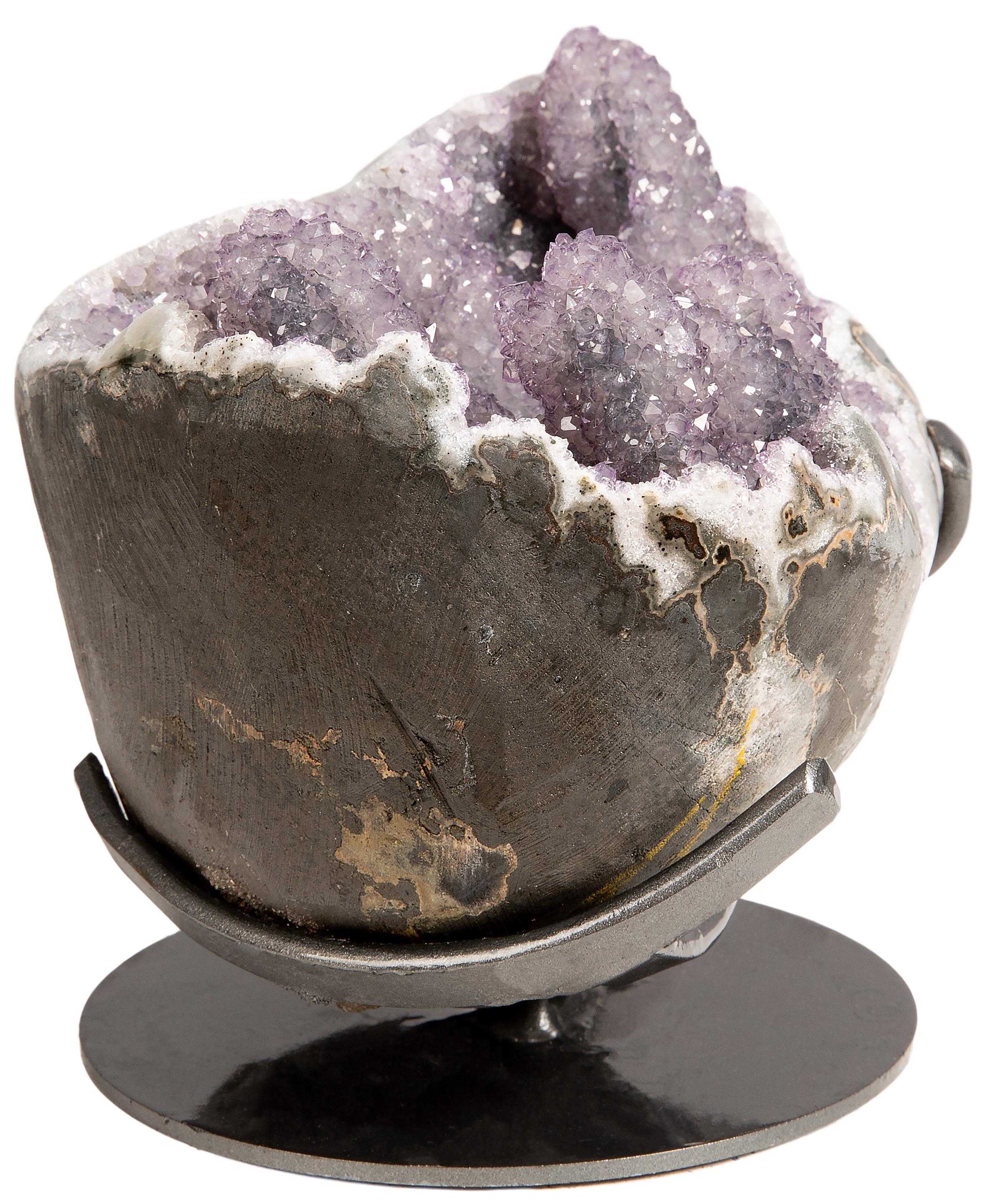 Questo splendido pezzo è un'ametista viola chiaro/lilla con formazioni stalattitiche uniche, presentata come un mezzo geode ipnotico su un elegante supporto decorativo in metallo. I bordi di questo bellissimo pezzo mineralogico sono stati lucidati,