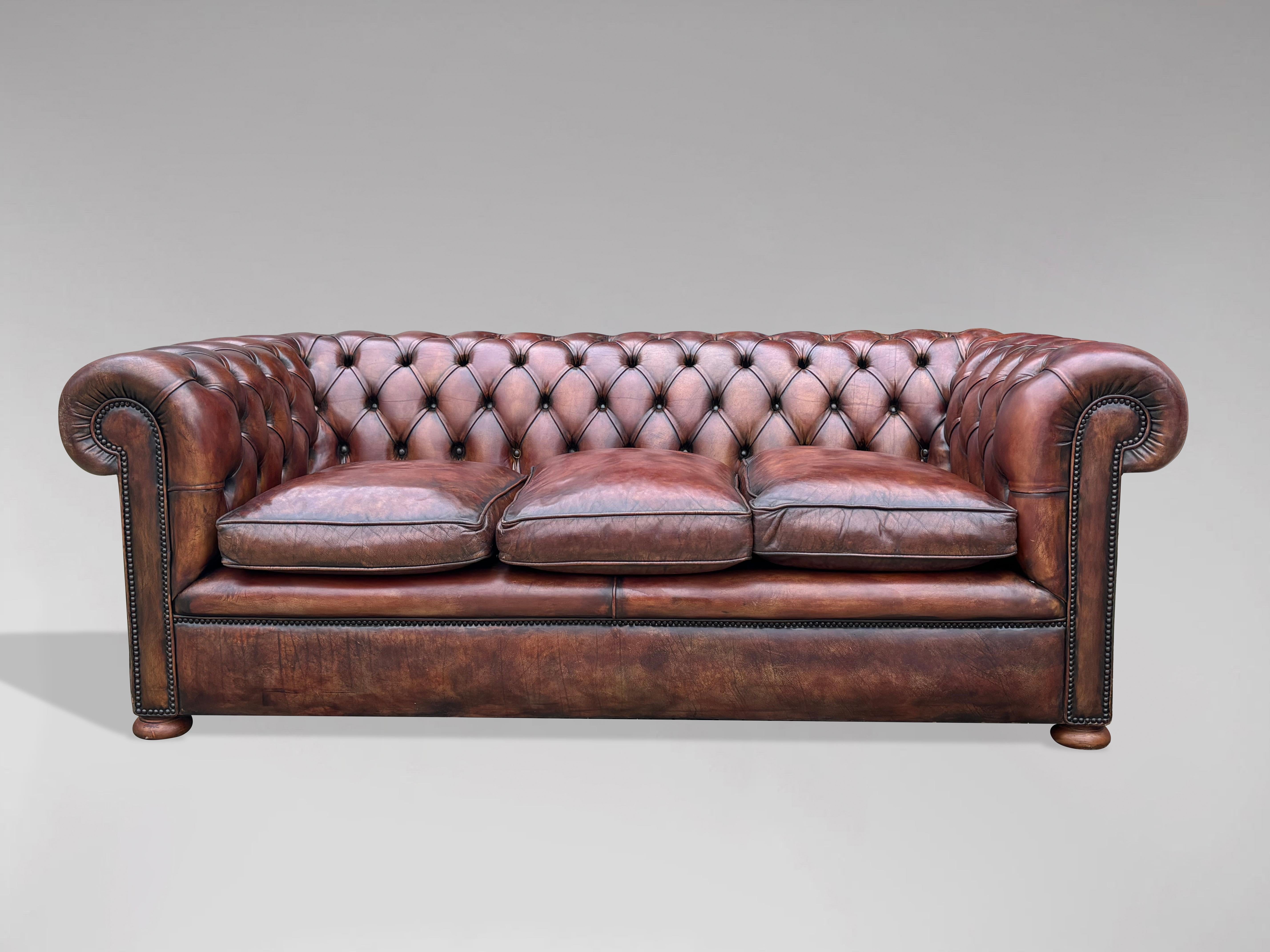 A stunning quality early 20th century large three seater brown leather chesterfield with three loose feathered cushions, raised on mahogany bun feet. With individually hand tacked brass studded trim. A fine example of a good quality with a good