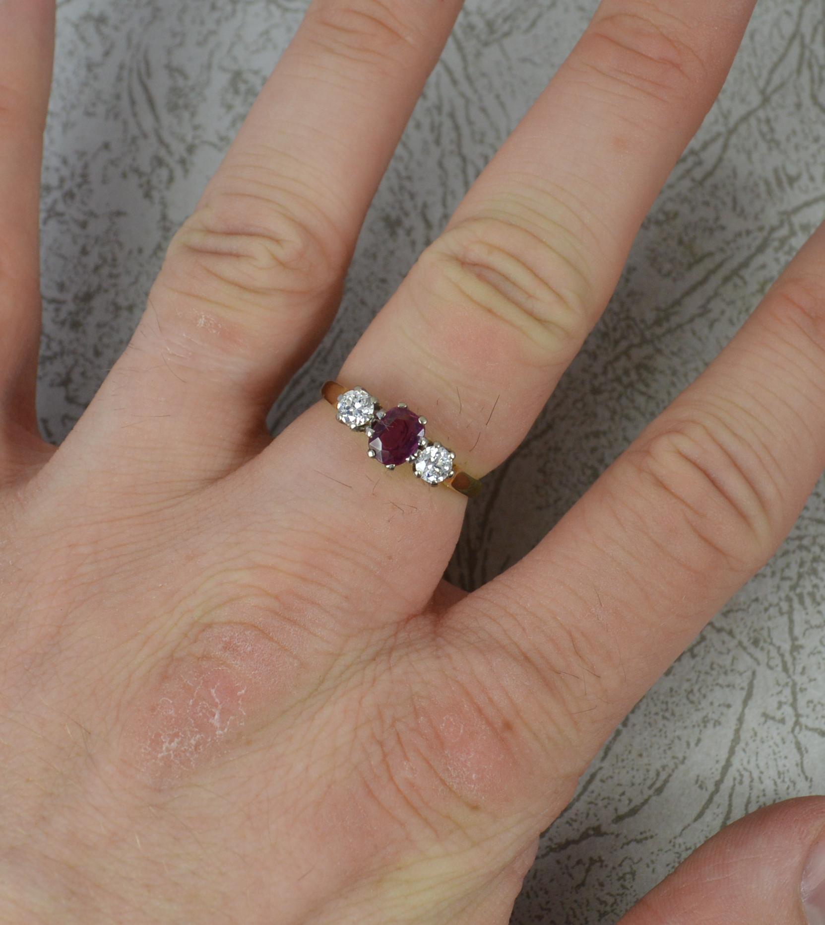 A ruby and diamond trilogy ring.
Solid 18 carat yellow gold example with platinum head setting.
Designed with a natural oval cut ruby gemstone to centre. High quality, likely untreated. 4.5mm x 5.7mm. To each side is a natural round brilliant cut