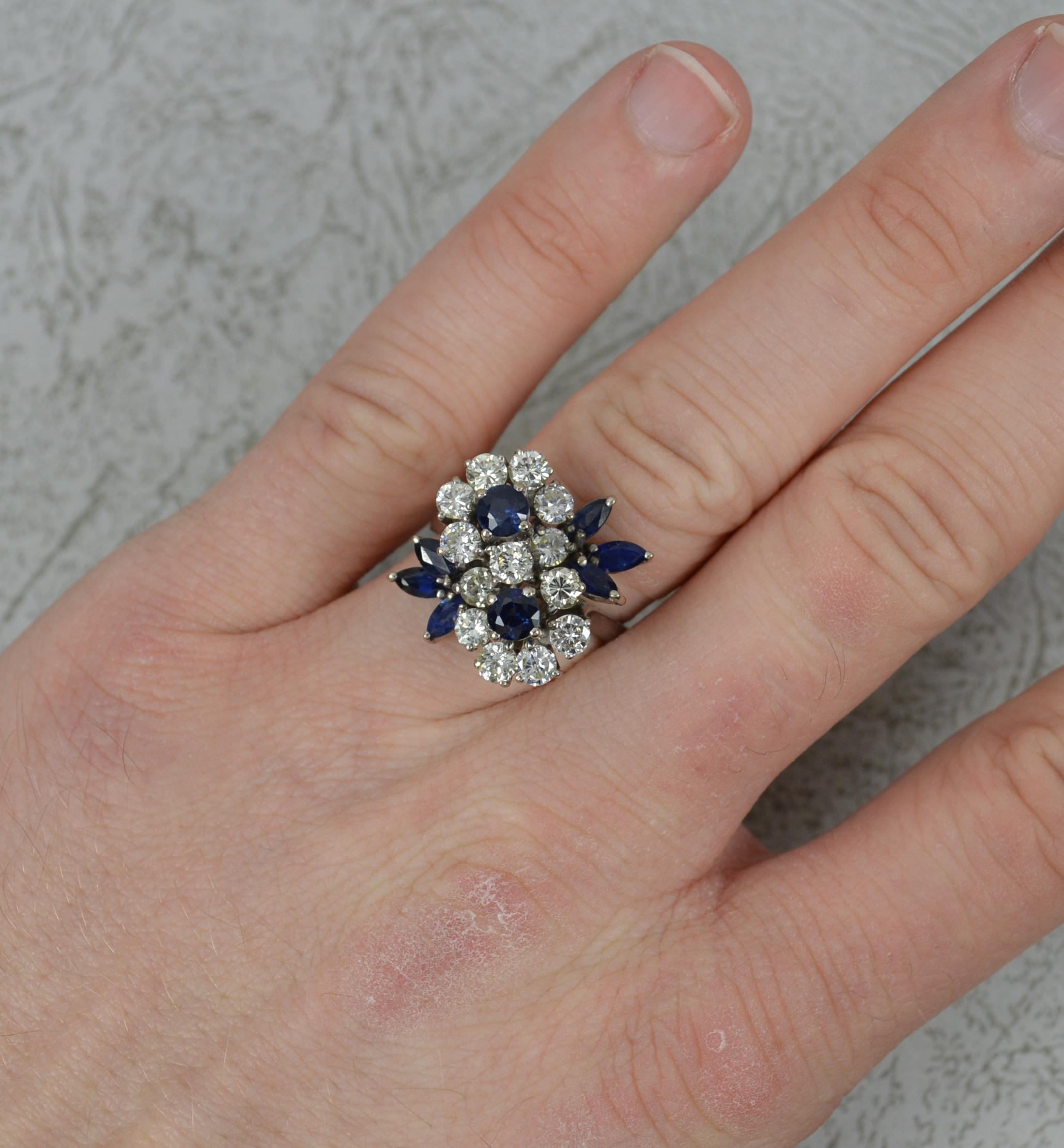 A superb quality vintage double flower cluster ring.
Solid 18 carat white gold example.
Designed with two round cut blue sapphires with full borders of bright round brilliant cut diamonds and three marquise cut blue sapphires to each side. A total