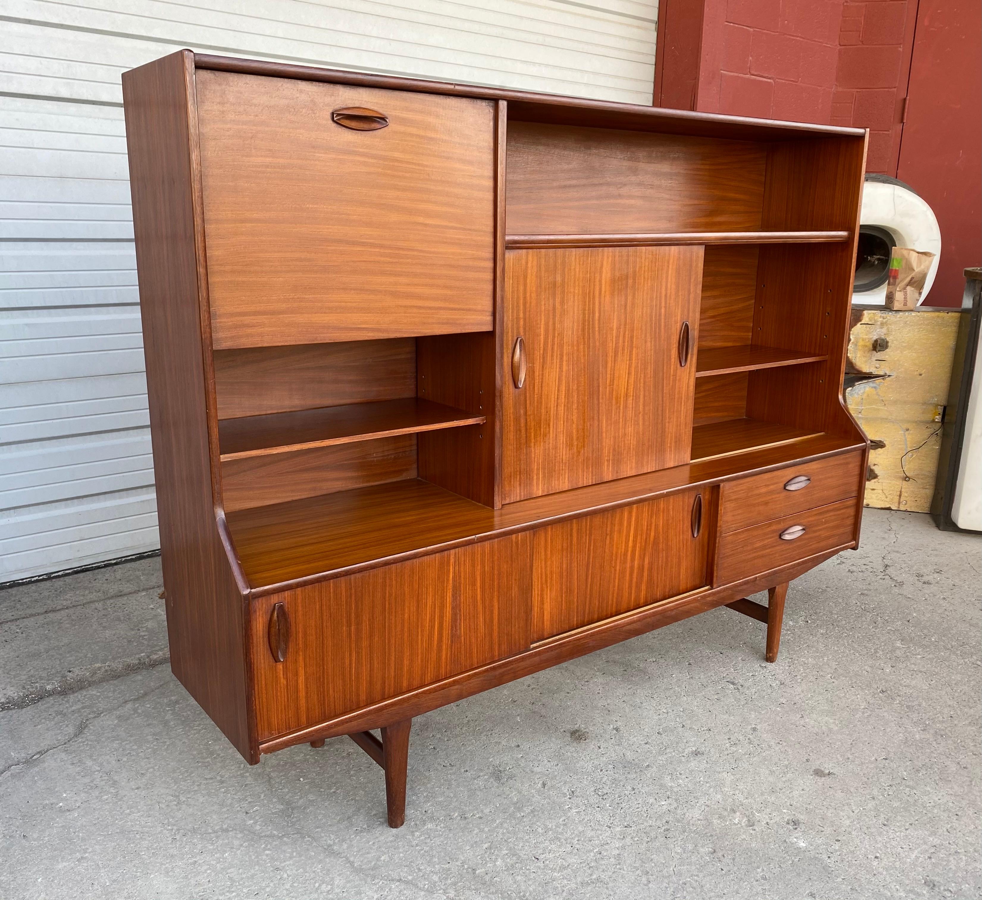 Stunning Scandinavian Modern teak high credenza/ server/bar, Classic design, great quality and construction, featuring generous storage, shelves, silverware drawer. Drop-down bar, hand delivery avail to New York City or anywhere en route from