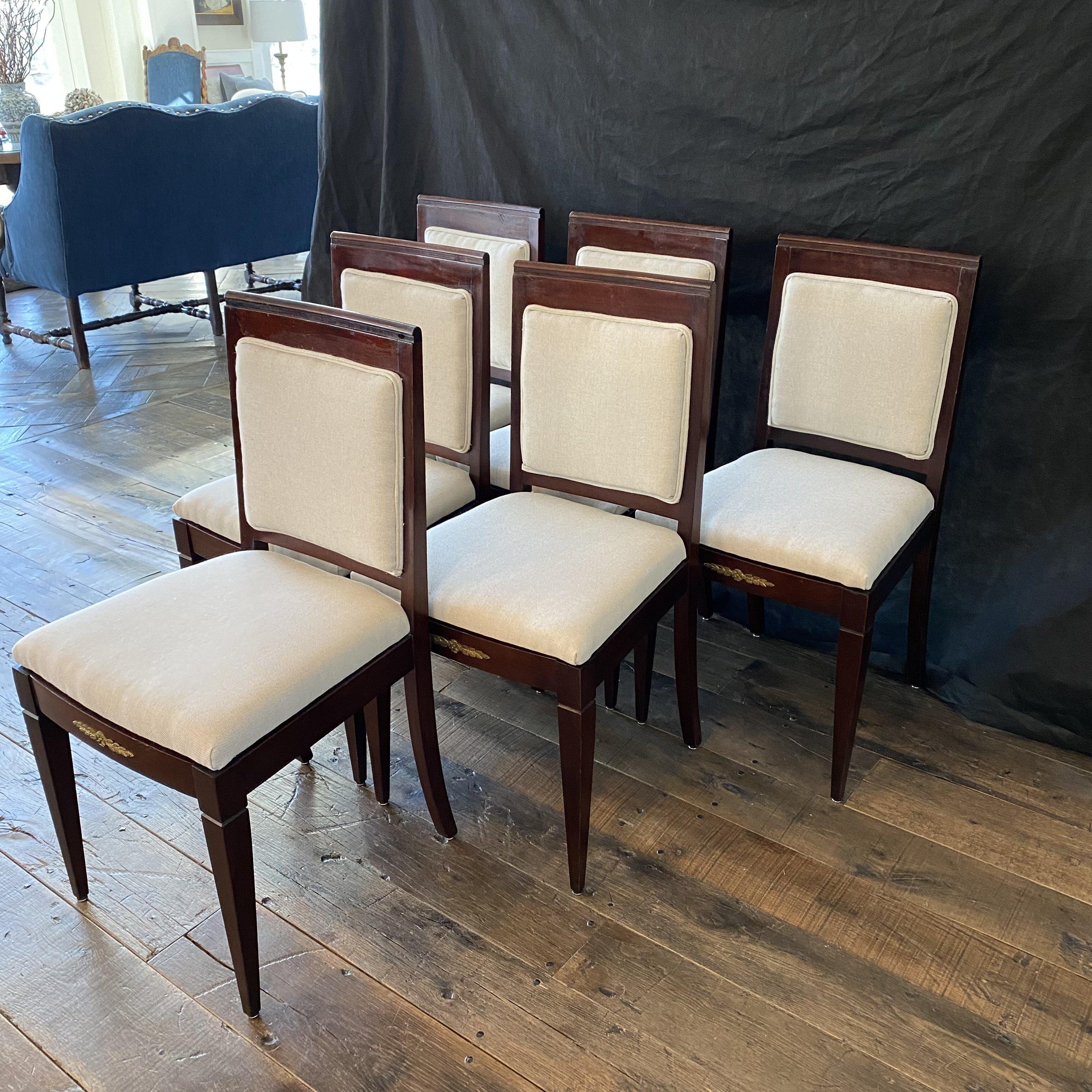 Elegant and sophisticated set of six French Empire style fauteuil side dining chairs are crafted from mahogany with ormolu mounts and new cream upholstery. The chairs feature tapering square profile legs and aprons decorated with neoclassical ormolu