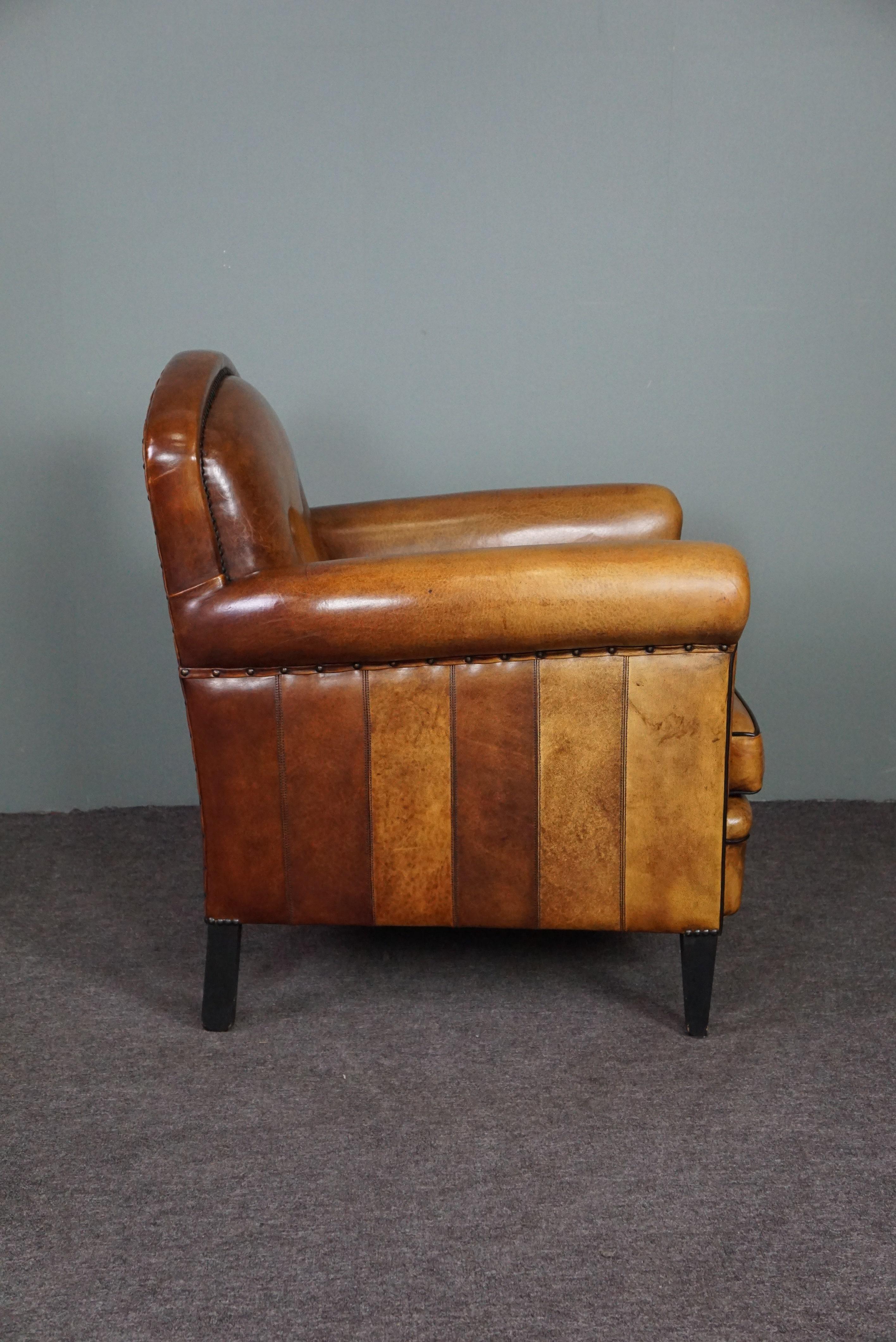 This well-colored sheepskin armchair/armchair has a striking drawing in the leather, is comfortable to sit on and is beautifully finished with decorative nails, black piping and stands on slender, sleek black wooden legs. Characteristic of this