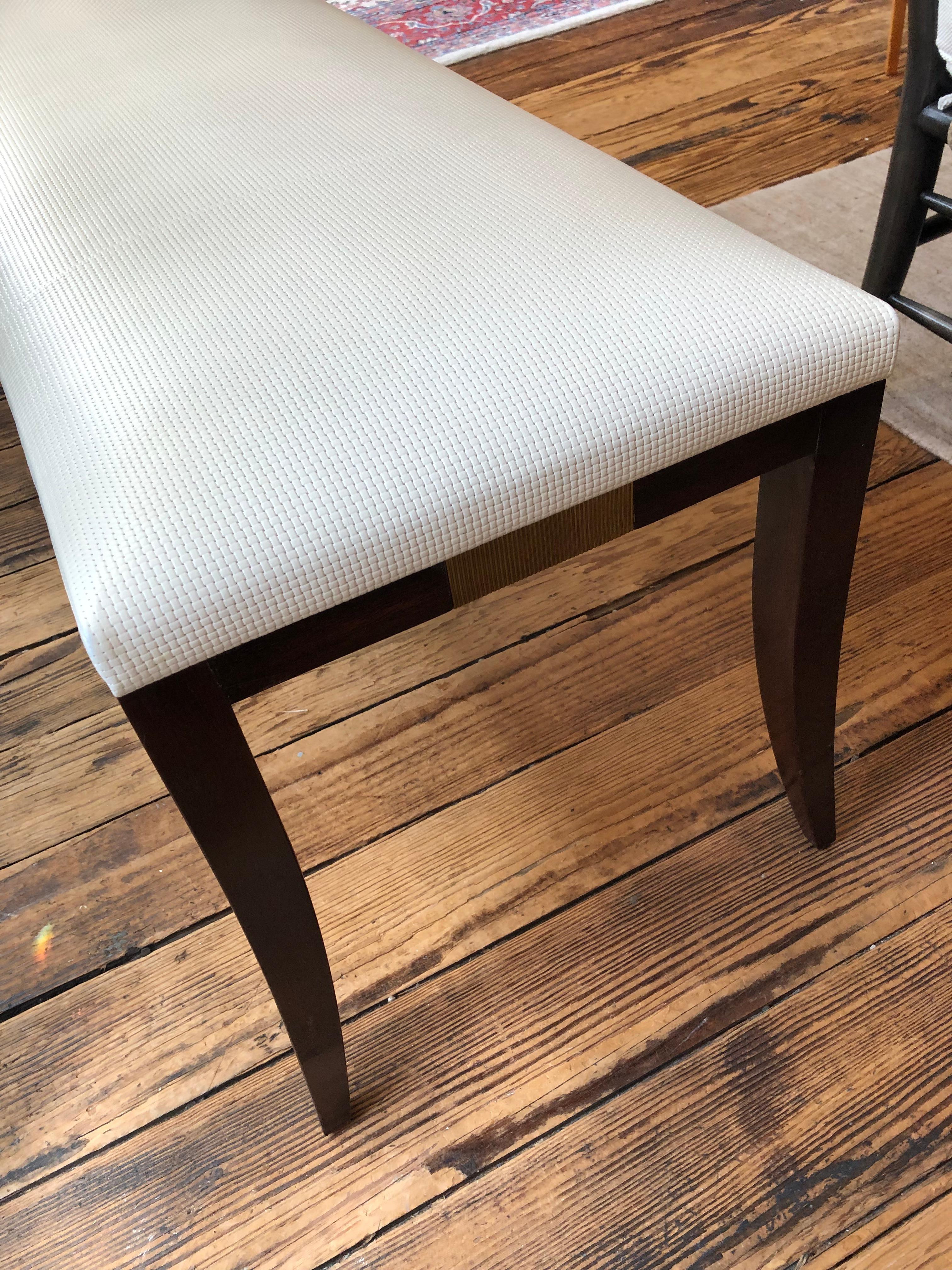 Sophisticated and sleek contemporary bench by Baker having mahogany slightly splayed tapered legs and base with handsome brass plaque decoration on each end. Upholstery is a chic woven polyester fiber.
