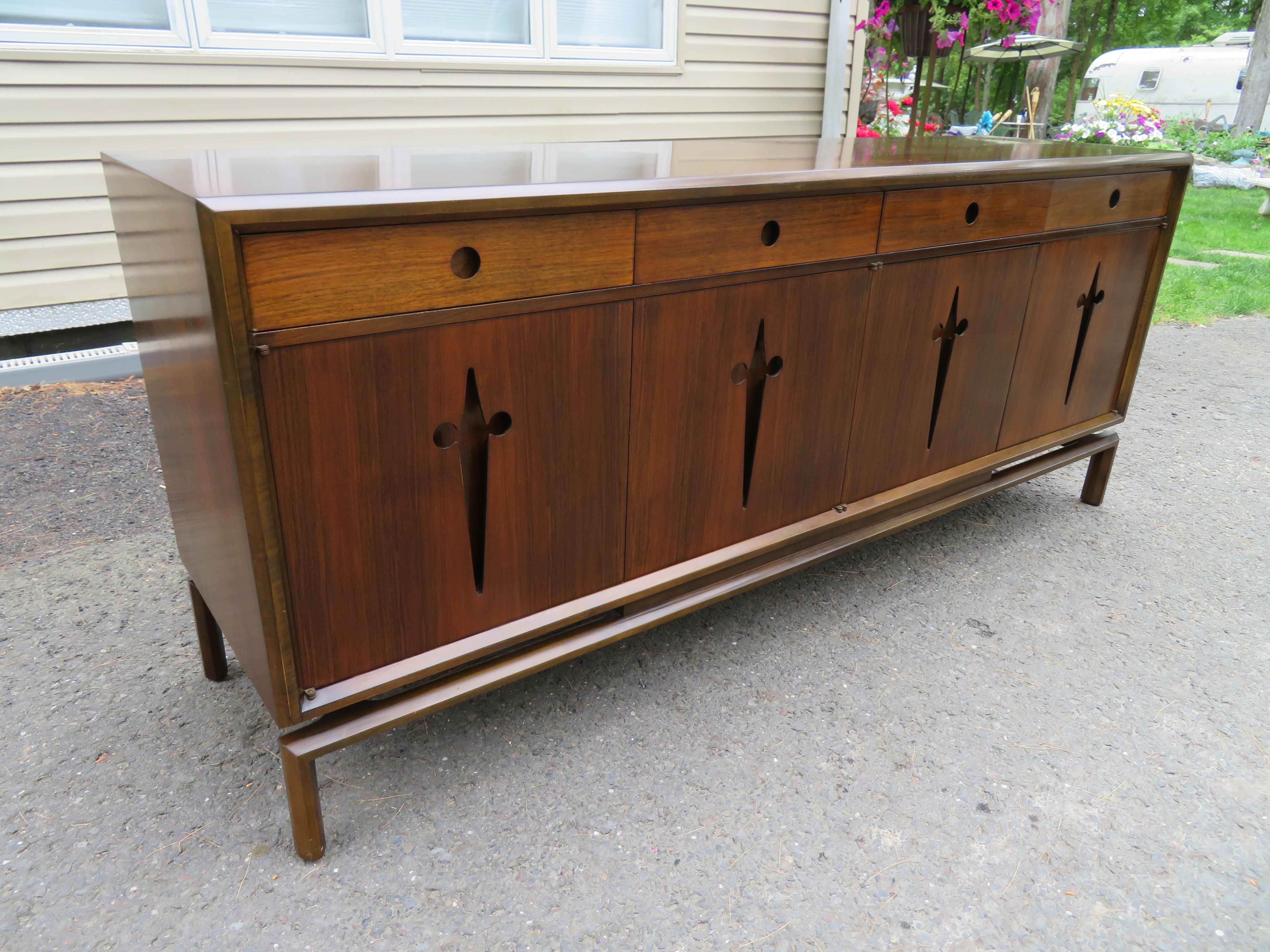 Stunning Edmond J. Spence walnut credenza manufactured in Sweden and features an easily recognisable high-quality construction. The four hinged cabinets open via handles of cut-out crucifixes. The cabinet itself is given a gentle floating feeling