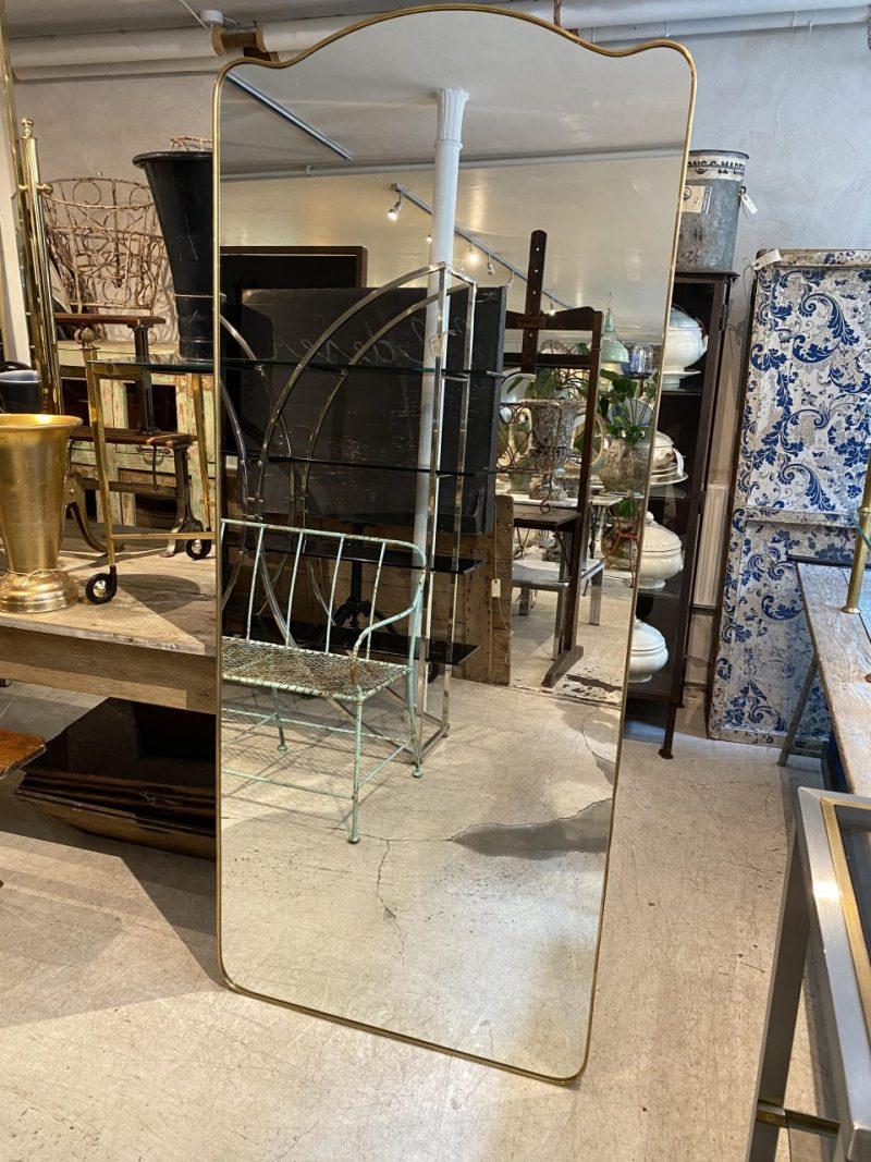 Stunning and imposing tall midcentury brass mirror from circa 1960s Italy. It has a sleek and tight quality brass frame with a rounded profile, and super hints of a princess style top in its curved rectangular form.

Original mirrored glass, and