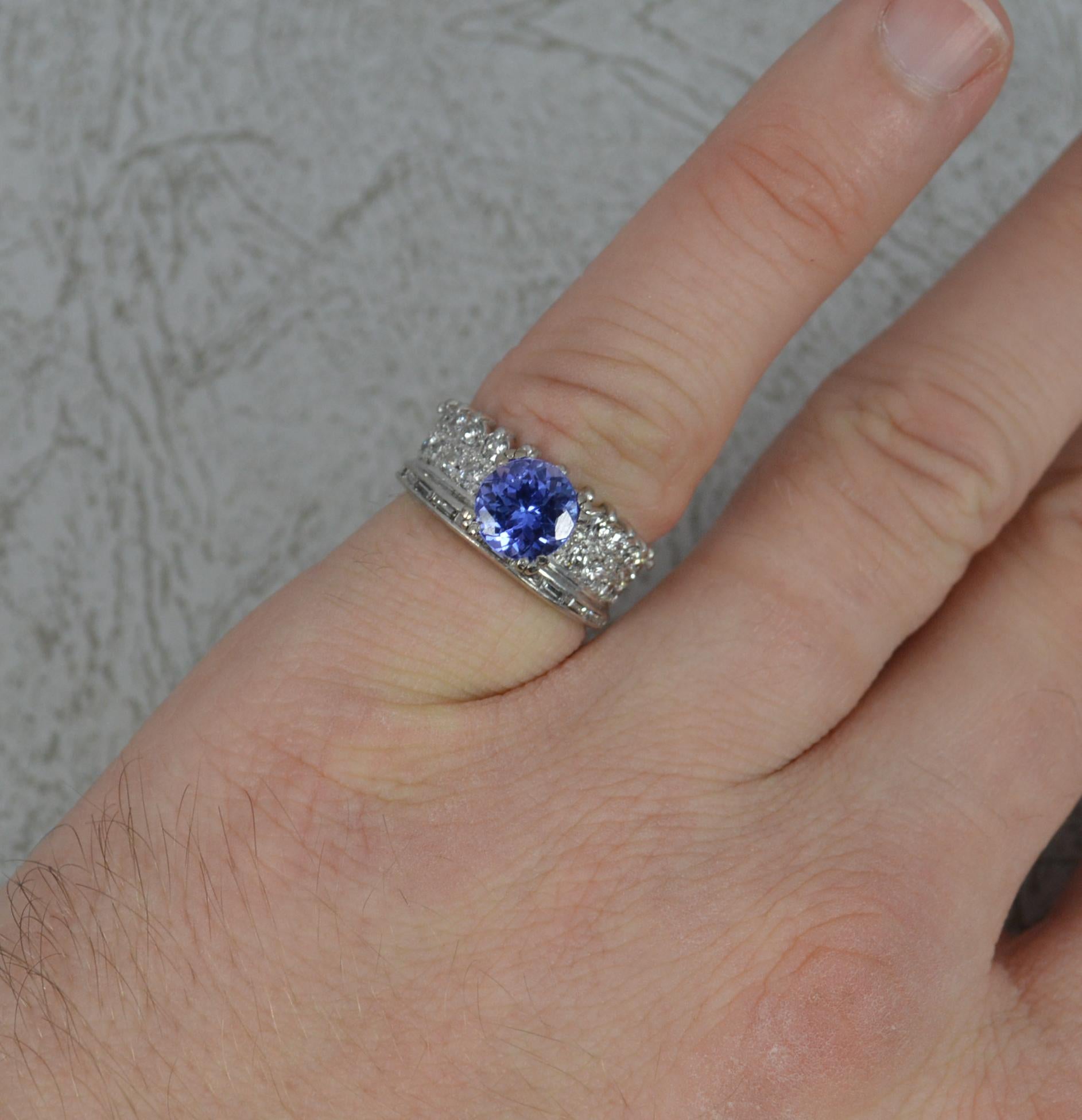 A wonderful cluster ring.
Solid 18 carat white gold example.
Set with a single round cut tanzanite to centre in a four triple claw setting. 7mm diameter.
Twenty seven round brilliant cut and eleven baguette cut diamonds surrounding to help form a