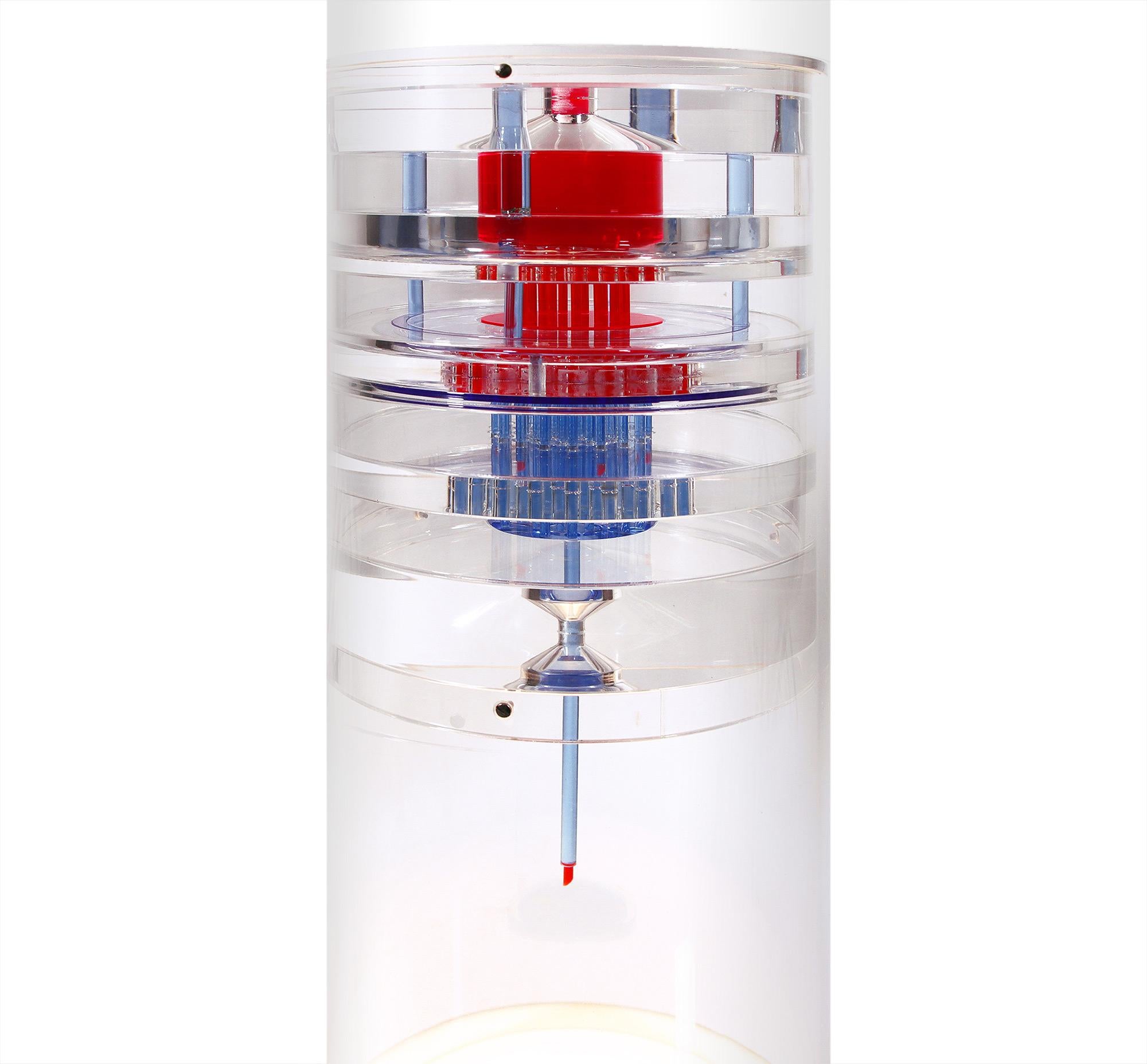 Unique piece made of a thick plexiglass column with red and blue elements inside, a metal base and illuminated from below with a circular fluorescent tube.
The object is probably an exhibition piece and shows a model of a turbine, engine,