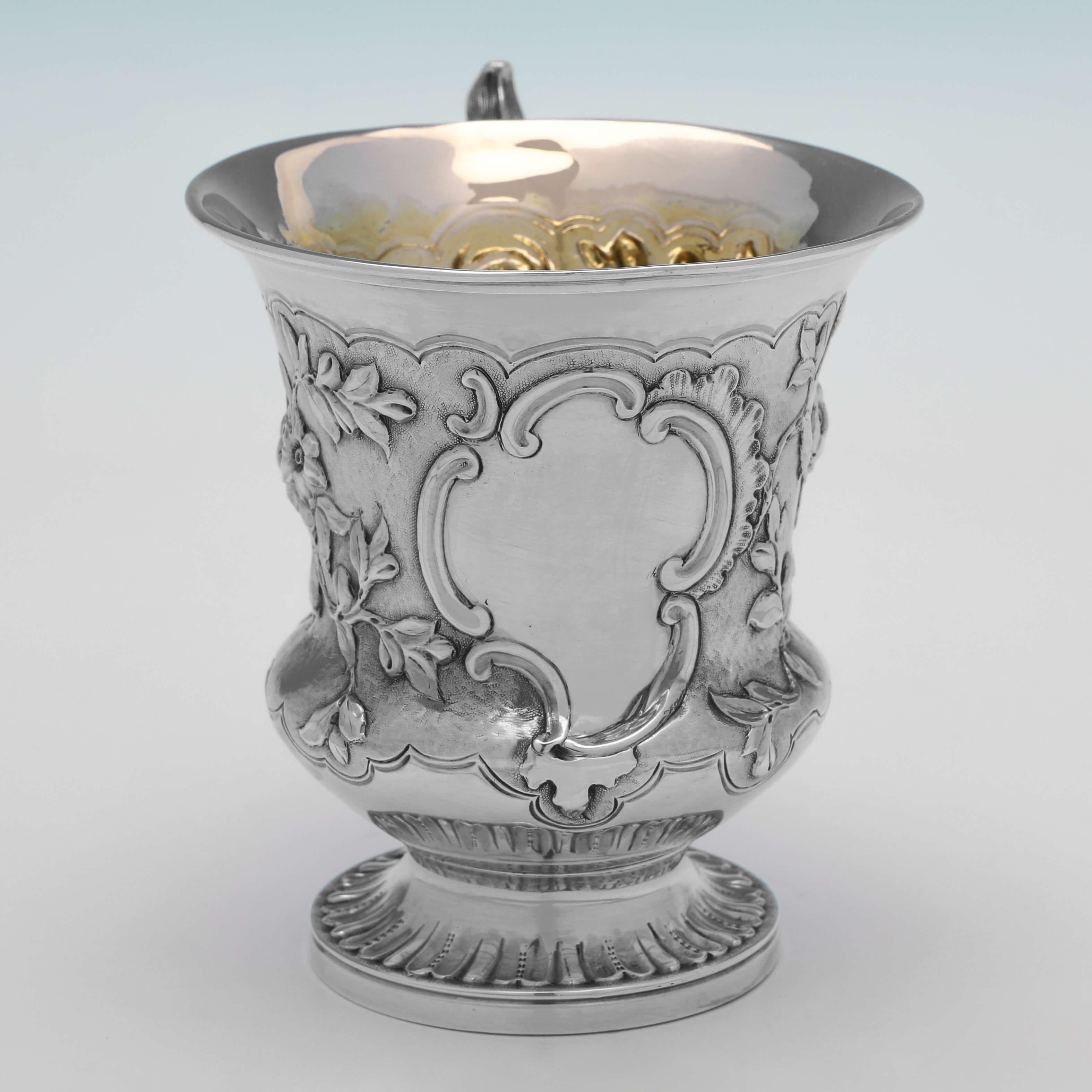 Hallmarked in London in 1840 by J. C. Edington, this attractive, Victorian, Antique Sterling Silver Christening Mug, features wonderful chased floral decoration to the body, an ornate handle, and a gilt interior. 

The christening mug measures