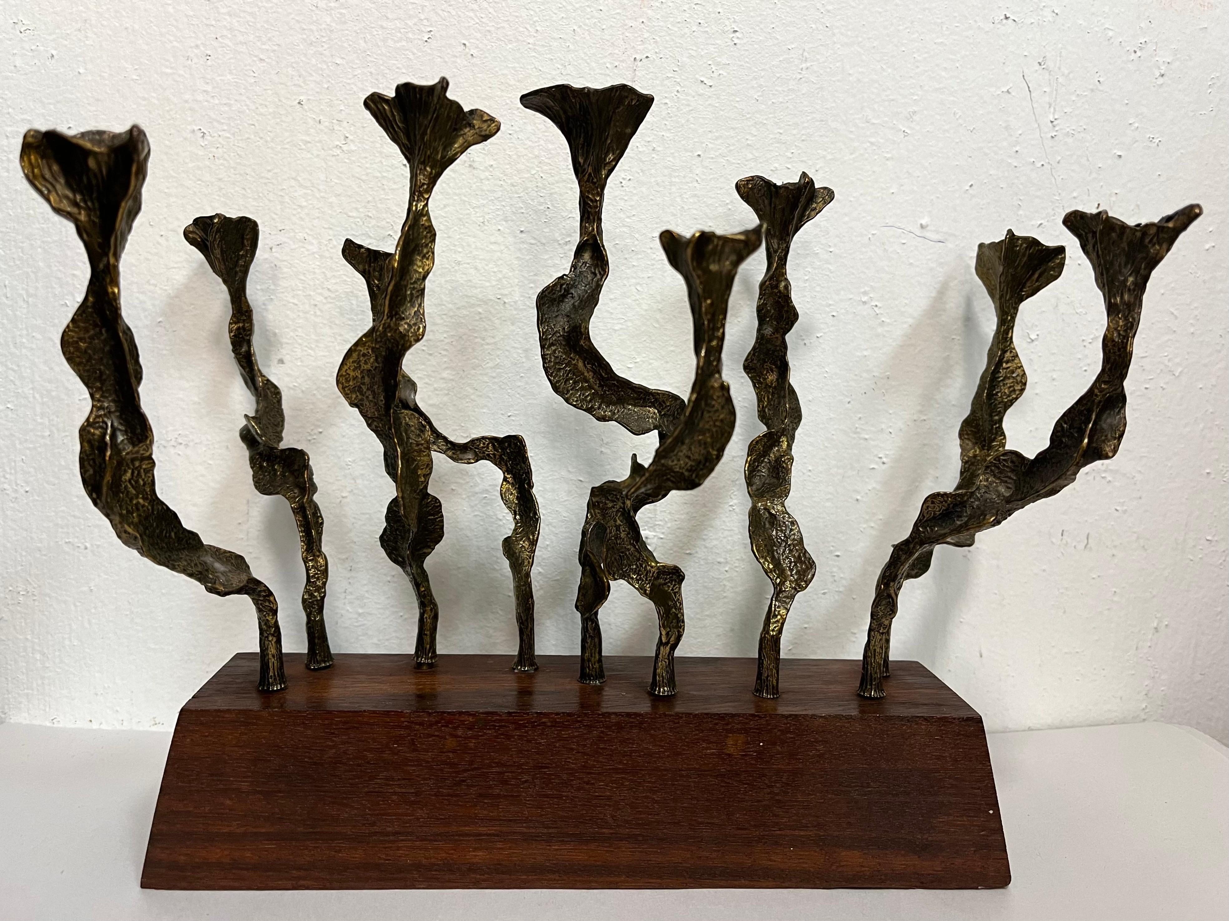 A vintage, circa 1970s Brutalist and quite sculptural Menorah crafted of bronze and wood by Israeli artist Menachem Berman. The individual candle holders are each unique and highly detailed. The plinth, trapezoidal style base of wood has clean,